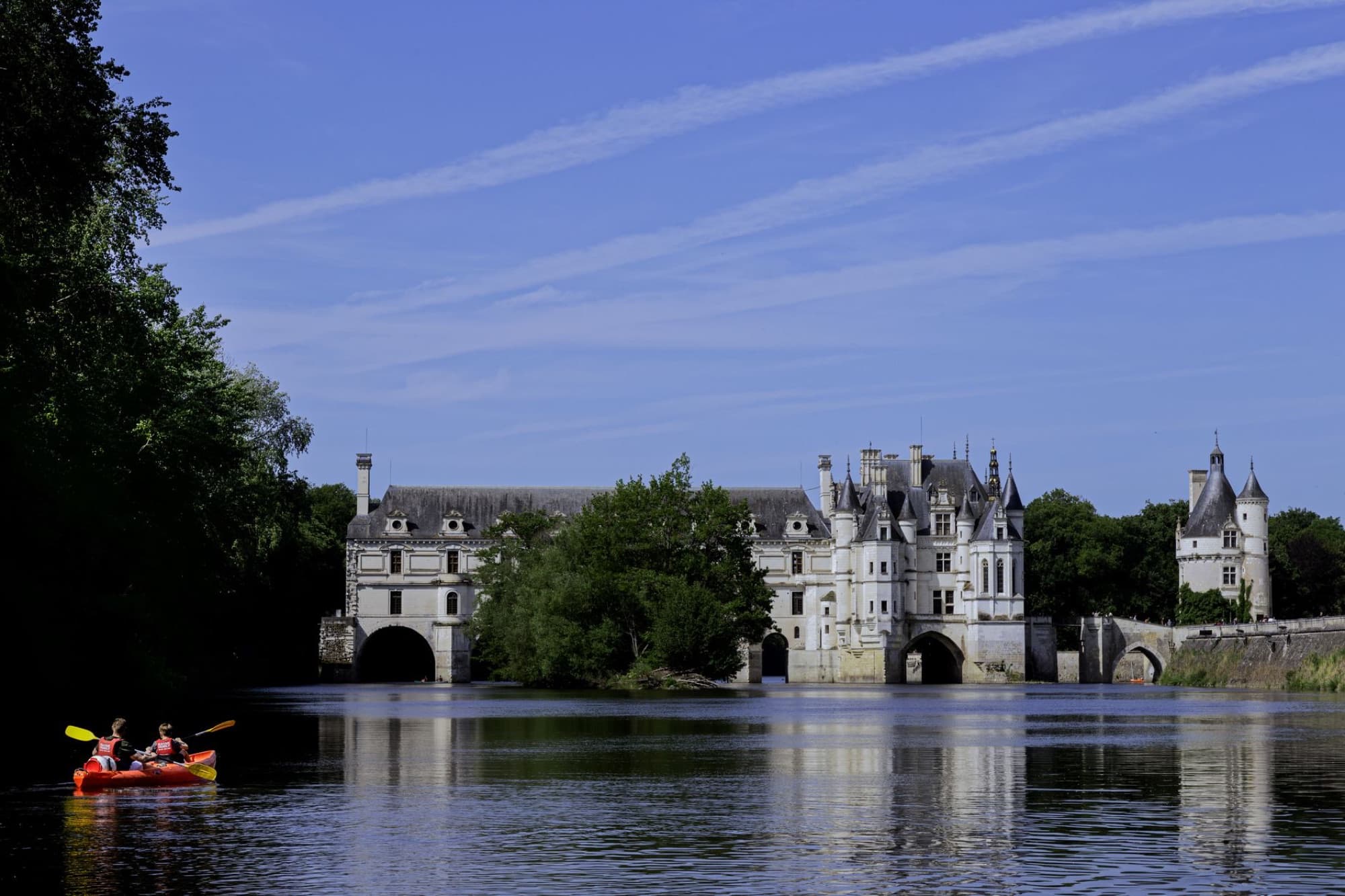 Scenic view of Château de Chenonceau reflecting on the Cher River with kayakers paddling nearby.