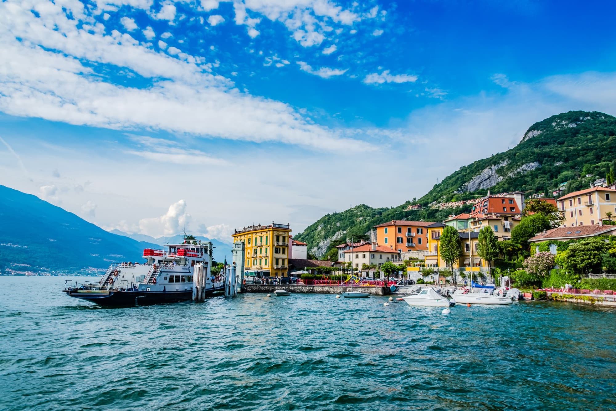 Scenic view of Lake Como's vibrant waterfront with mountains and boats in Lombardy, Italy.