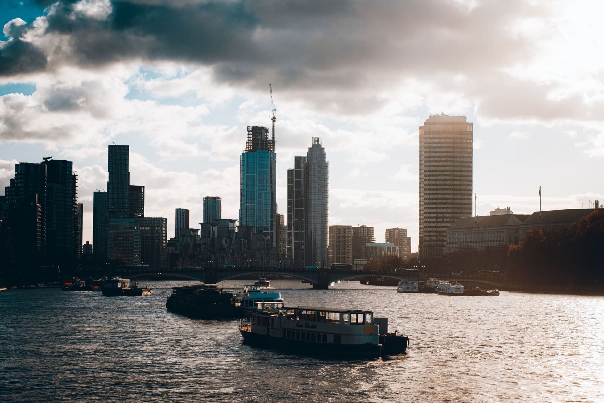 Scenic view of the London skyline at sunset, showcasing skyscrapers and boats on the River Thames.