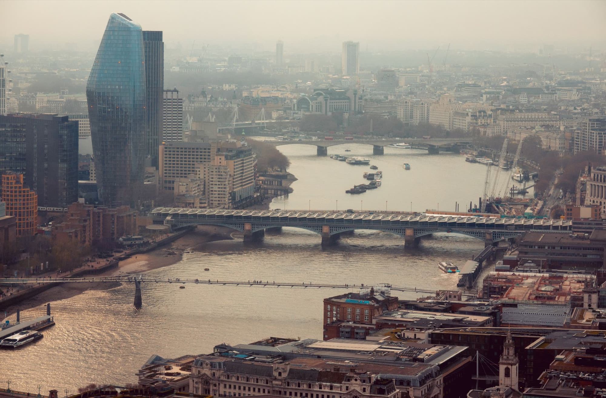Aerial view of London's cityscape featuring Thames River and iconic skyscrapers.