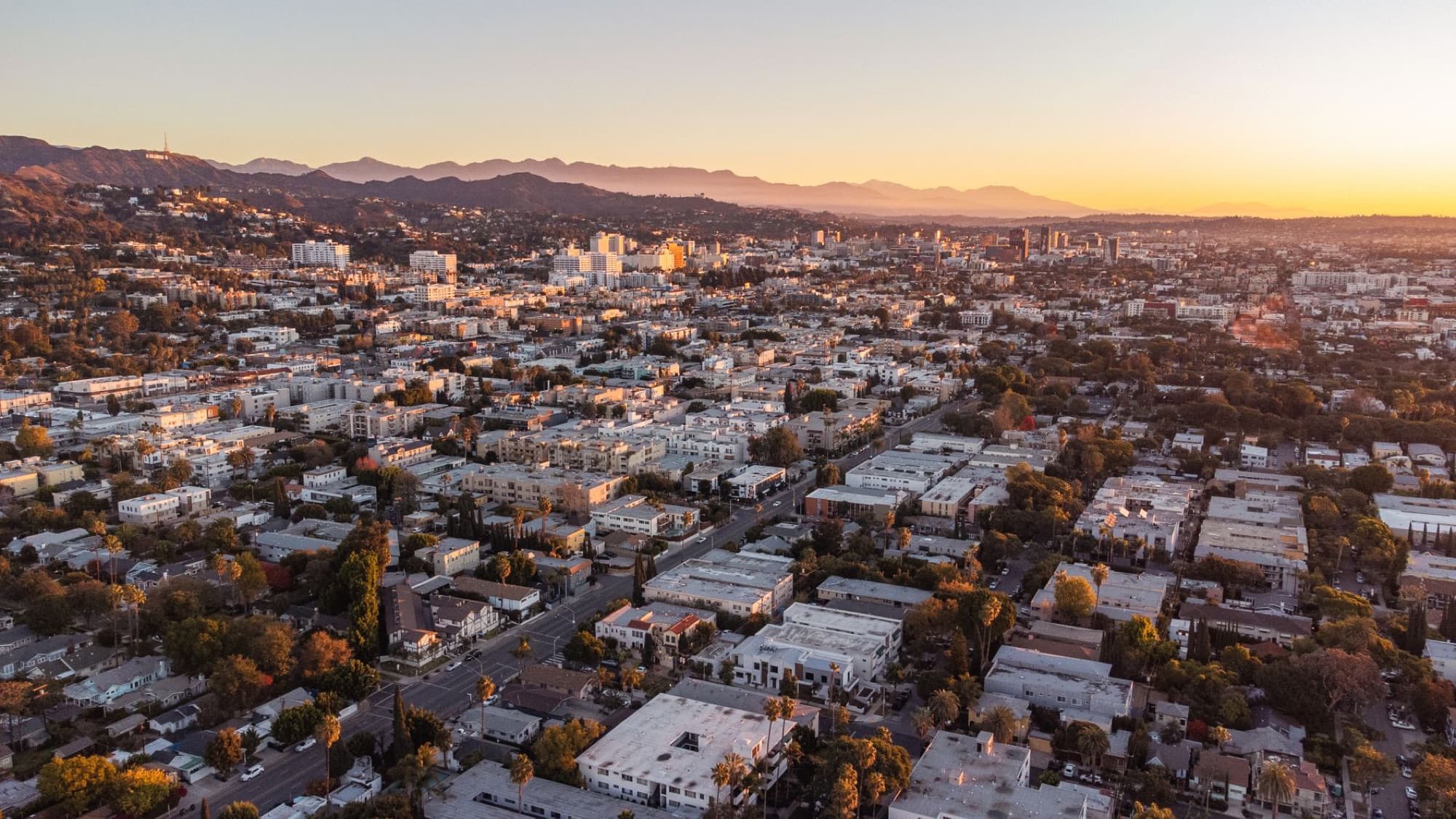 Drone shot of Los Angeles skyline and urban landscape at sunset.