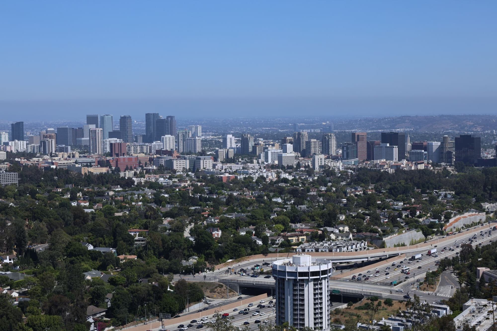 Aerial view of Los Angeles skyline, featuring busy highways and urban landscape under clear blue skies.