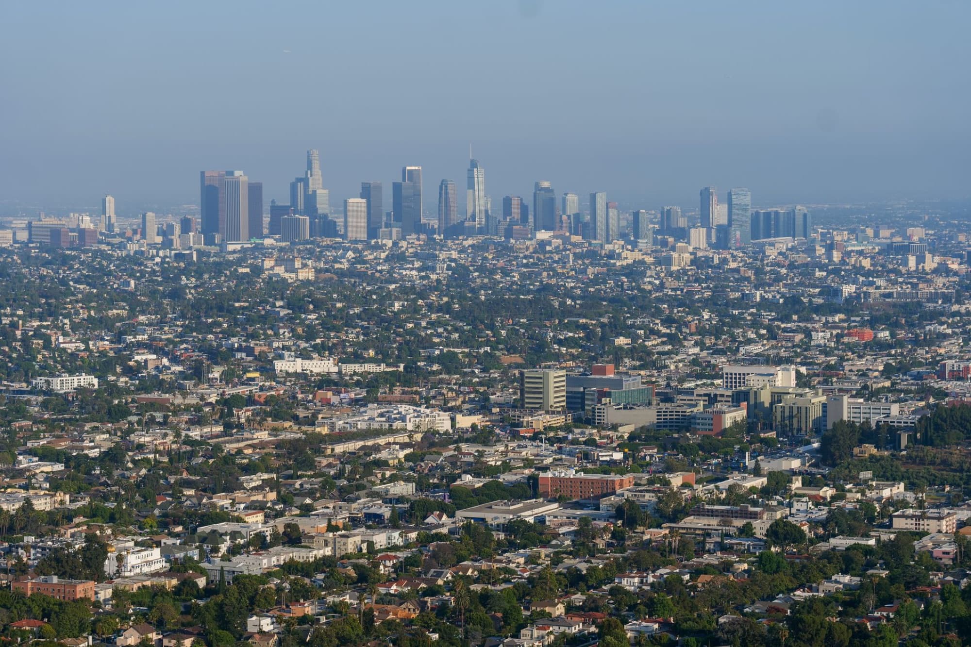 Expansive daytime aerial view of the Los Angeles skyline with numerous buildings and clear blue sky.