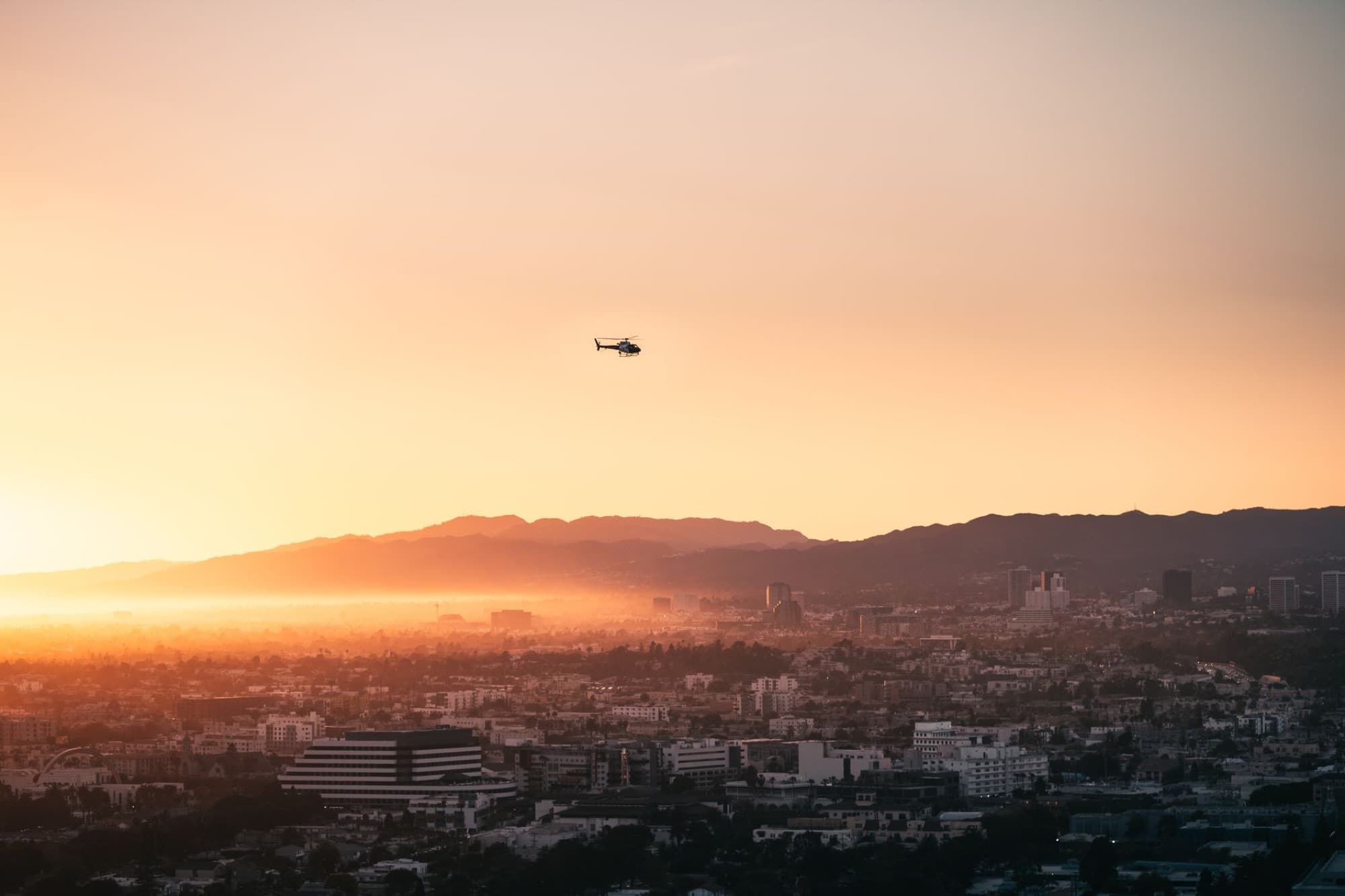 A breathtaking aerial view of Los Angeles with a helicopter flying at sunrise over the cityscape.