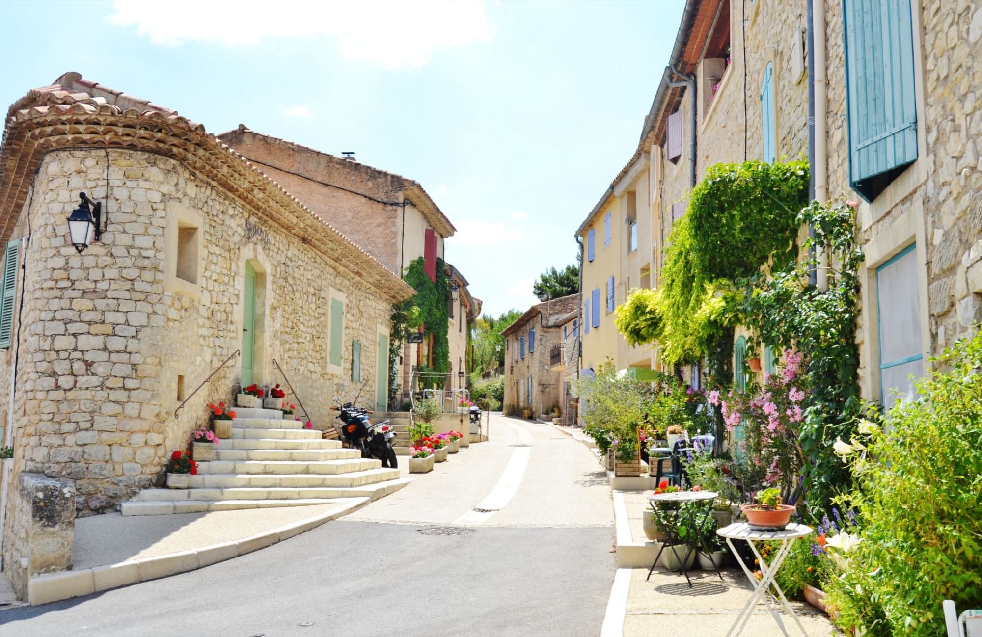 Picturesque street with stone houses and vibrant flowers in Vitrolles-en-Lubéron, France.