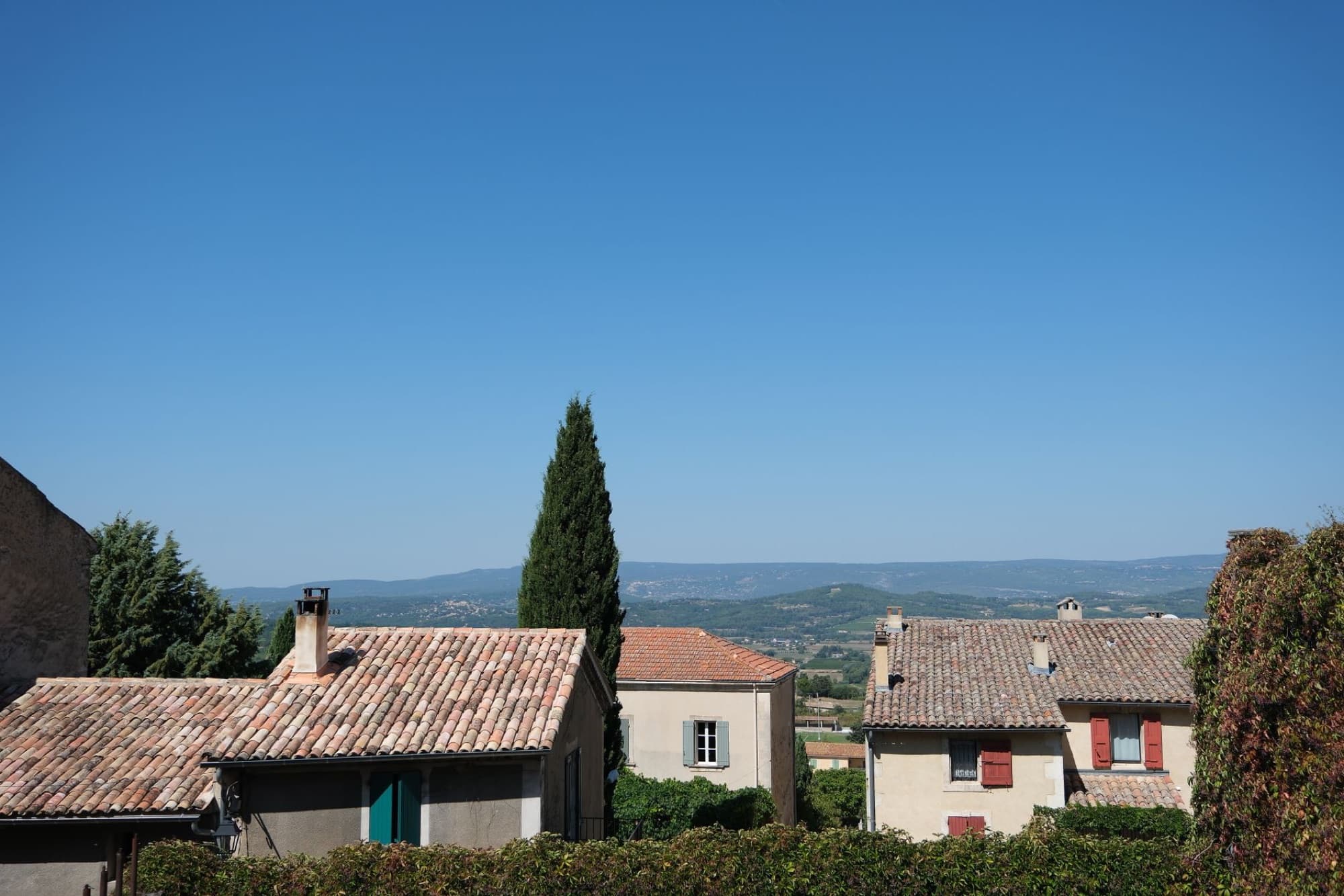 Scenic view of a quaint village nestled in a lush valley with mountain backdrop under a clear blue sky.