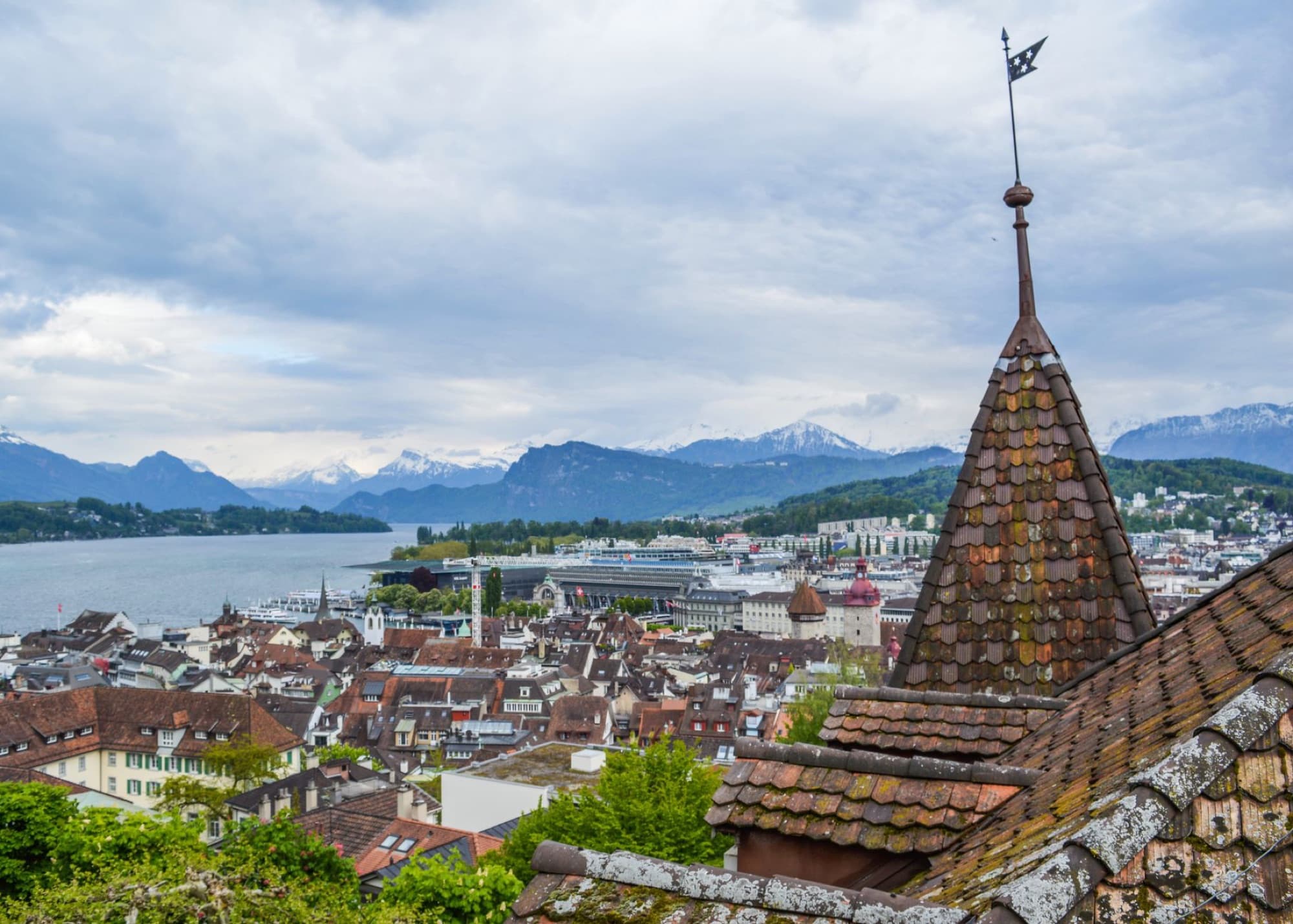 Old European town with aged residential buildings with tiled roofs located near river against mountains in cloudy day