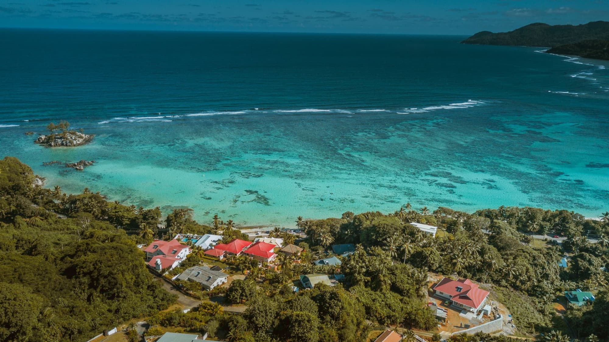 A breathtaking aerial view of a tropical island coastline with turquoise waters and lush greenery.