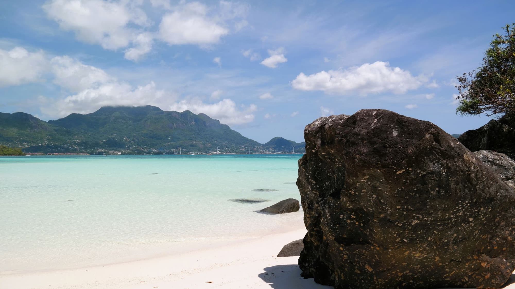 A stunning view of a tropical beach with clear waters, blue skies, and distant mountains.