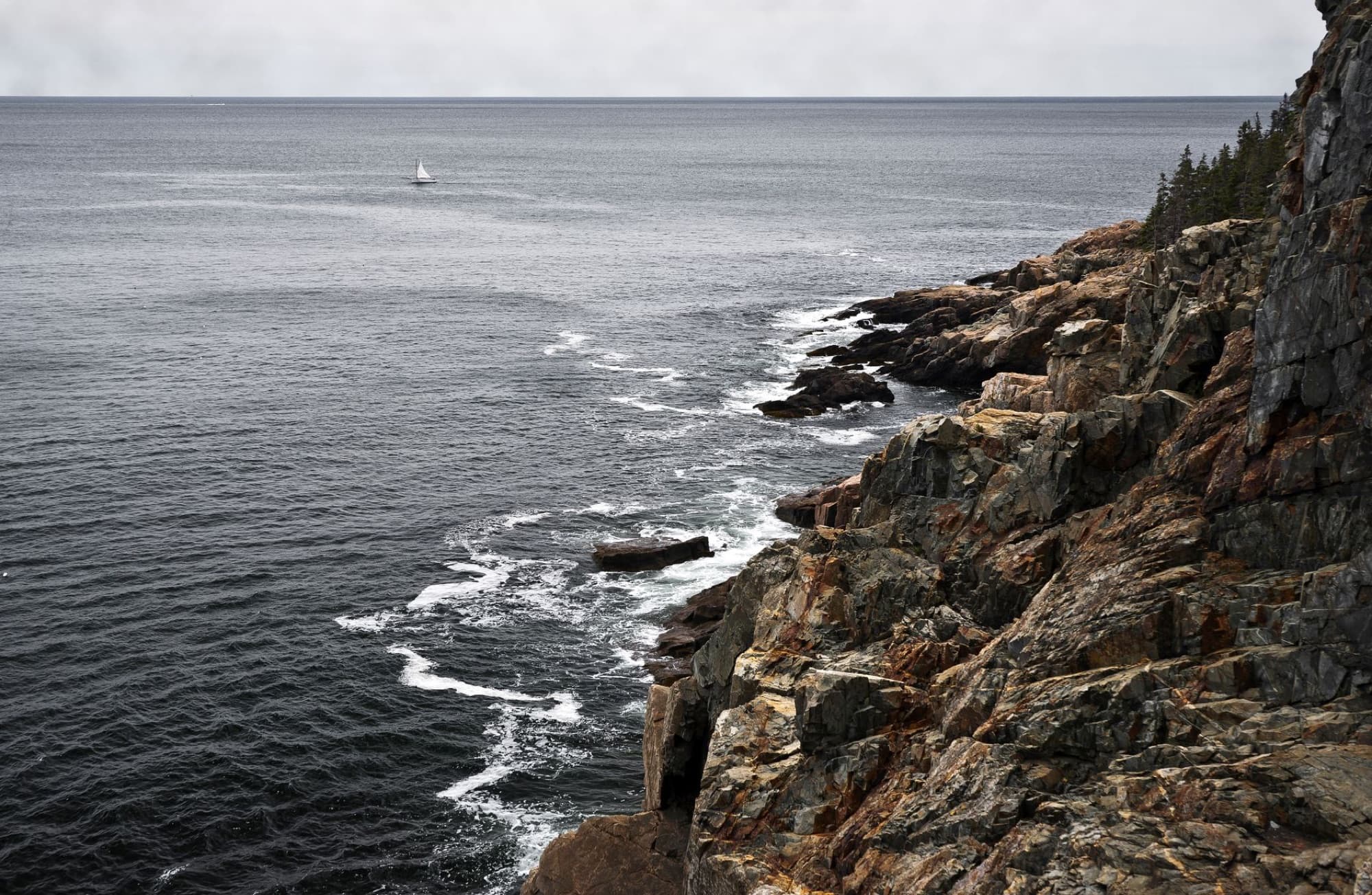 Majestic view of rocky cliffs and a sailboat on the ocean near Bar Harbor, Maine.