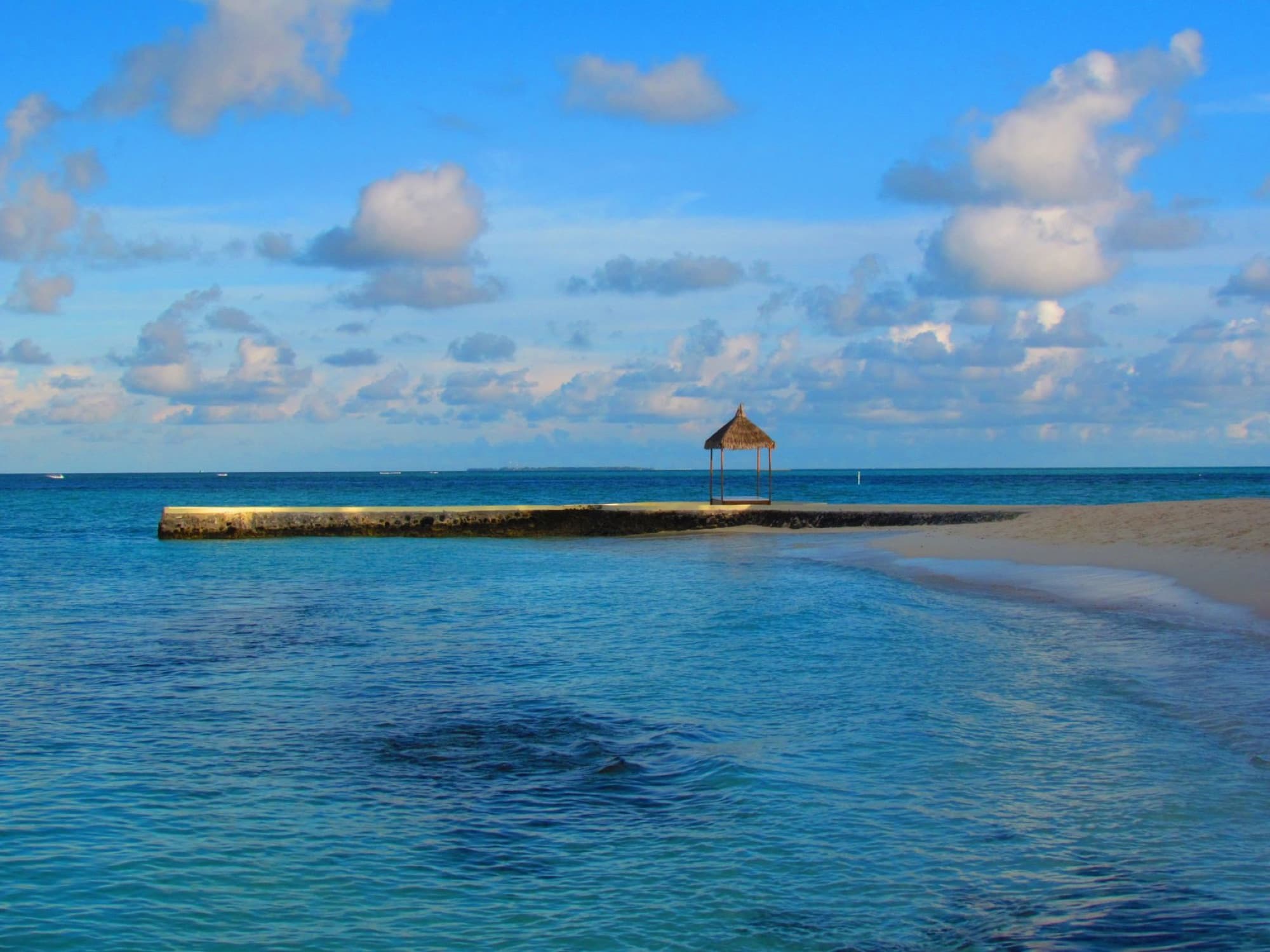 Tranquil beach scene in Maldives featuring clear blue waters and a thatched-roof gazebo.