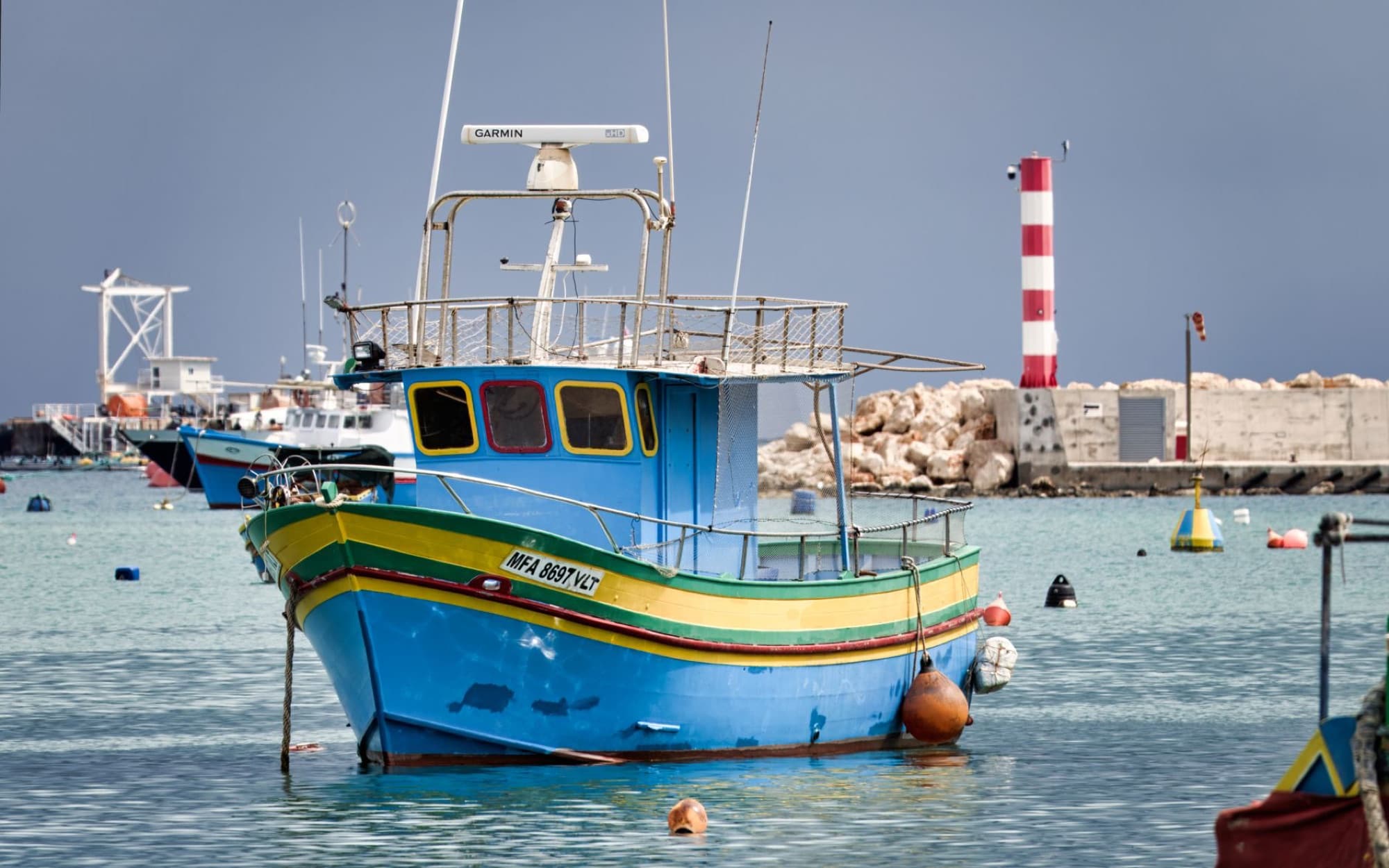 Vibrant traditional fishing boat in the serene Marsaxlokk harbor with scenic harbor view in Malta.