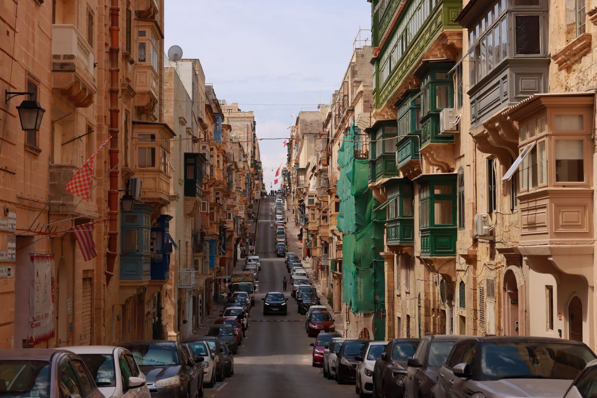 Vibrant city street in Malta lined with colorful buildings and parked cars under a clear sky.