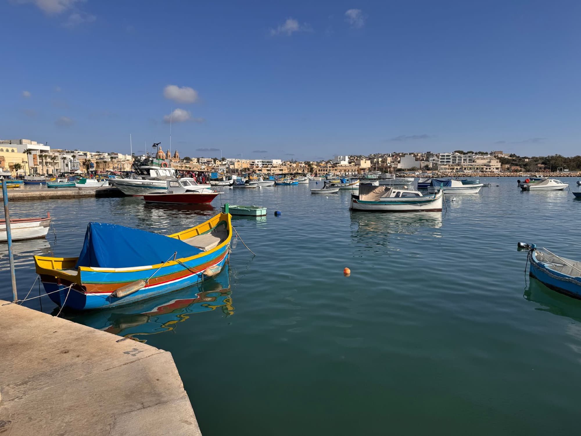 Vibrant traditional boats floating in the scenic Marsaxlokk harbor, Malta under a clear blue sky.