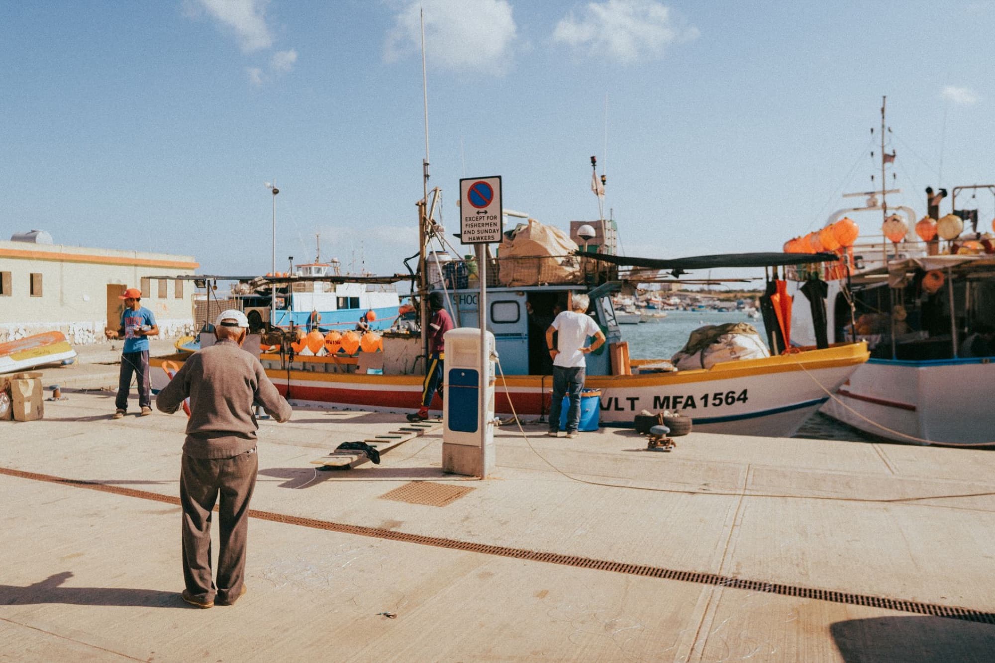 Fishermen working in the scenic Marsaxlokk harbor, Malta with colorful boats and clear blue skies.