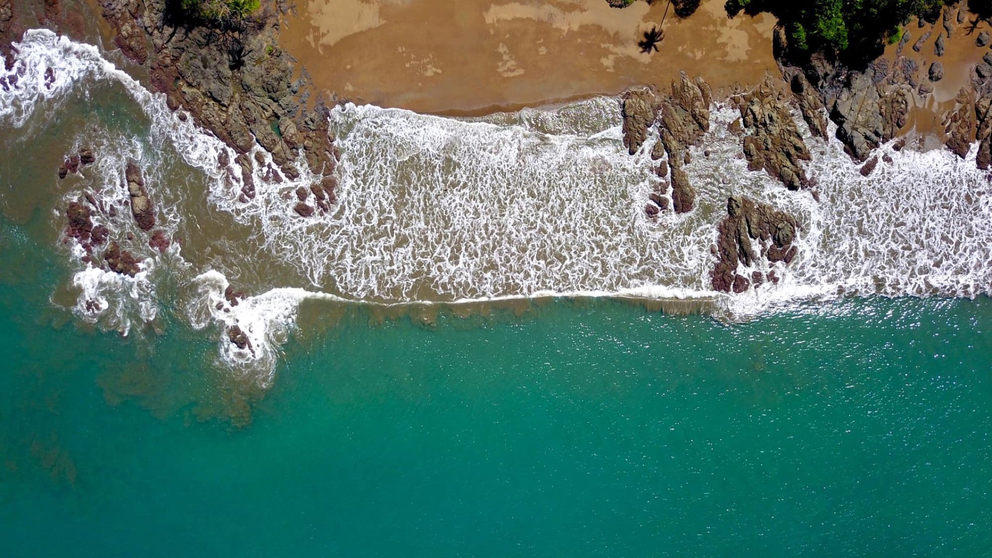 Stunning aerial shot of waves crashing on a rocky beach in Costa Rica's lush landscape.