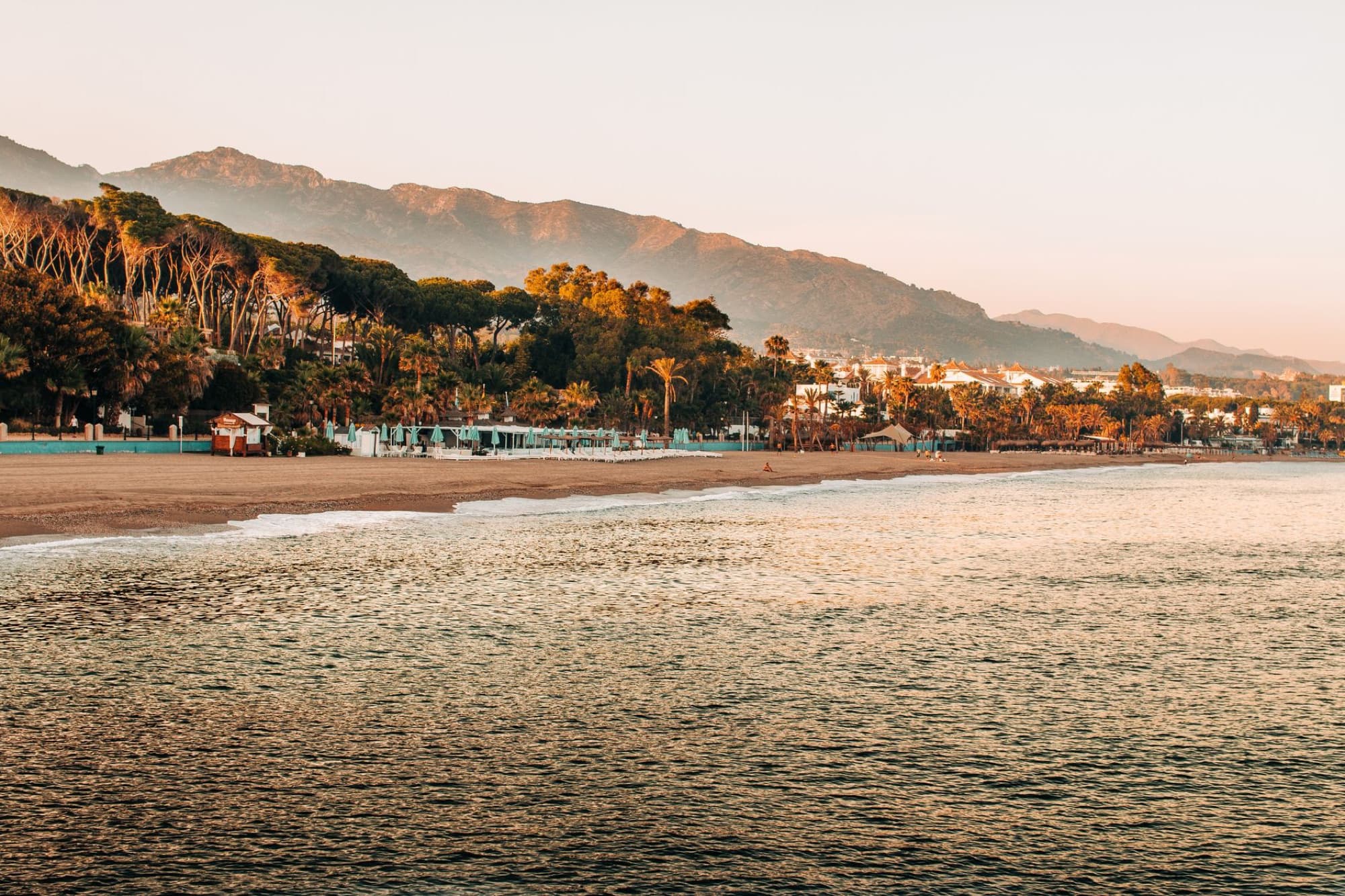 Peaceful sunrise view of Marbella's beach with mountains and lush greenery in Spain.