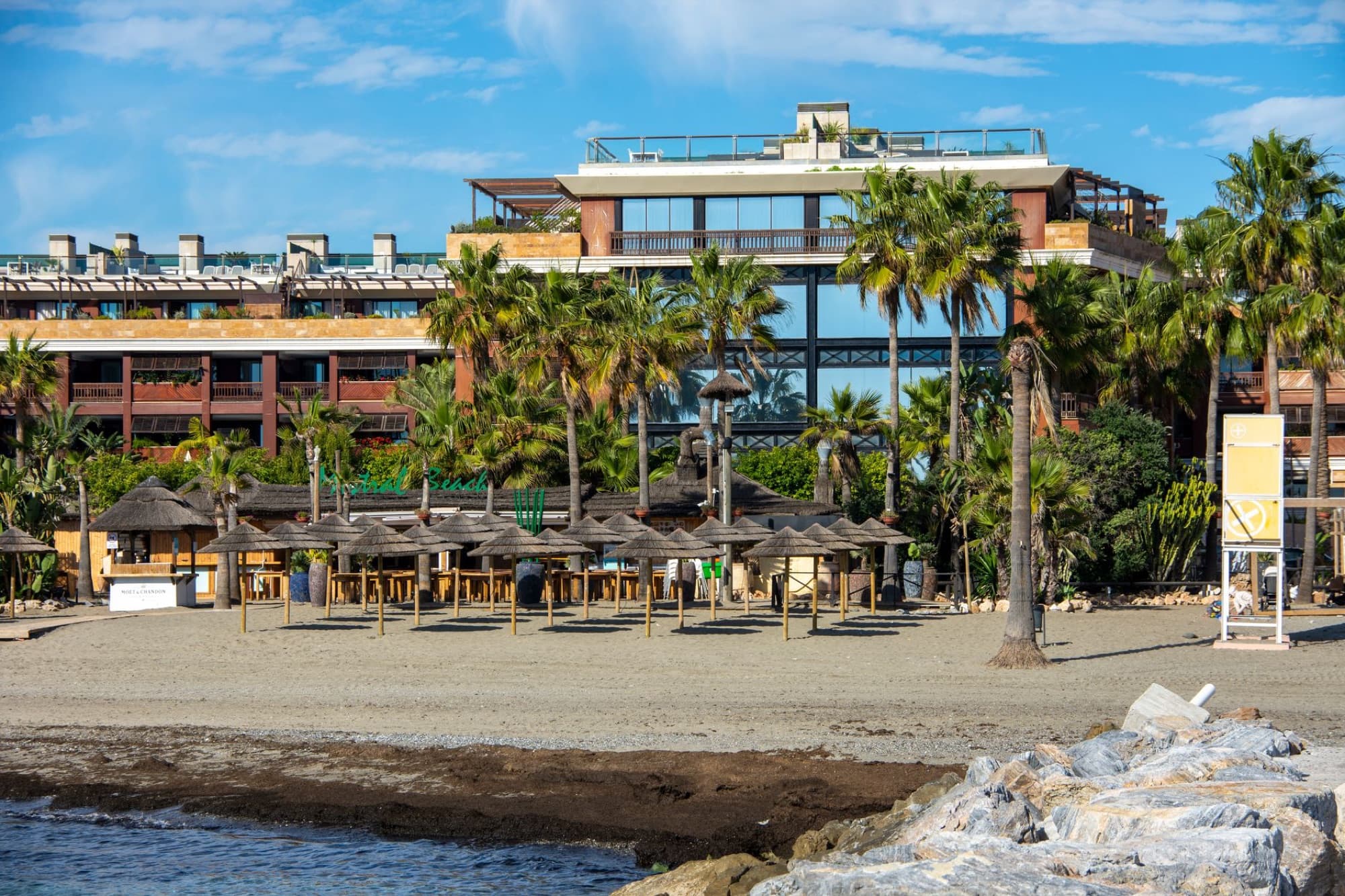 Scenic view of a beachfront building with palm trees and beach huts in Marbella, Spain.