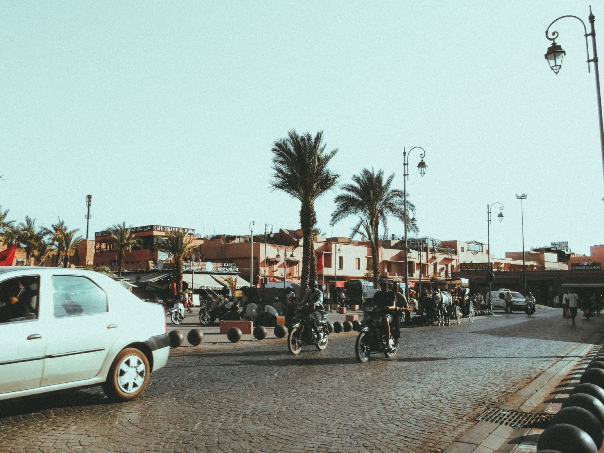 Lively street in Marrakech with motorbikes and palm trees under clear sky.