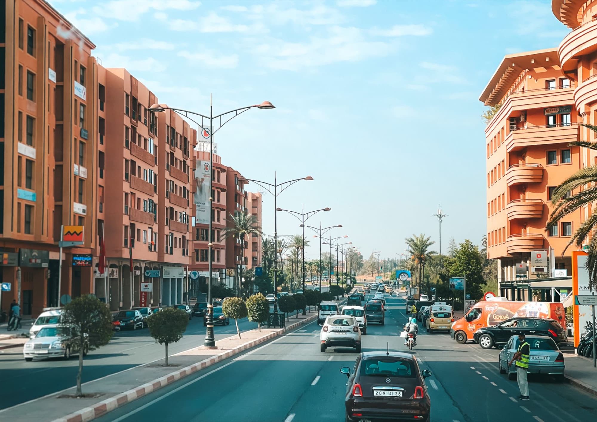 Vibrant street scene in Marrakech with traffic and distinctive architecture under a bright blue sky.