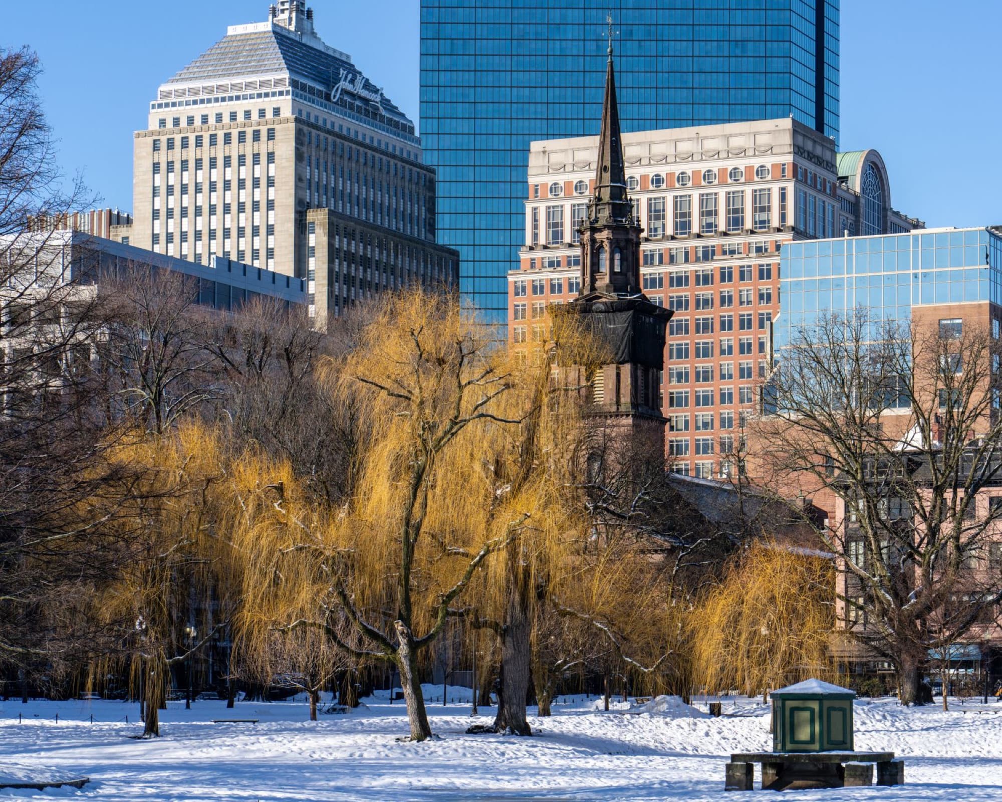 Snowy landscape with a historic church spire and modern skyline in Boston, Massachusetts.