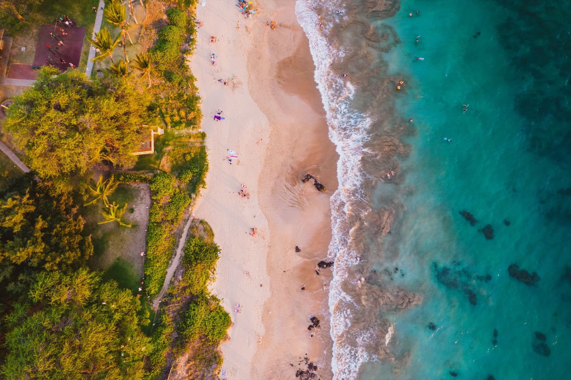 Stunning aerial view of a tropical beach with turquoise waters and golden sand in Maui, Hawaii.