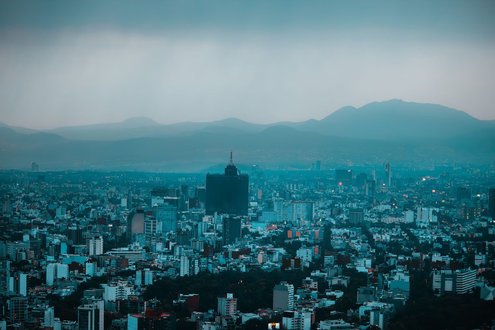 A dramatic aerial view of Mexico City skyline with mountains in the background.