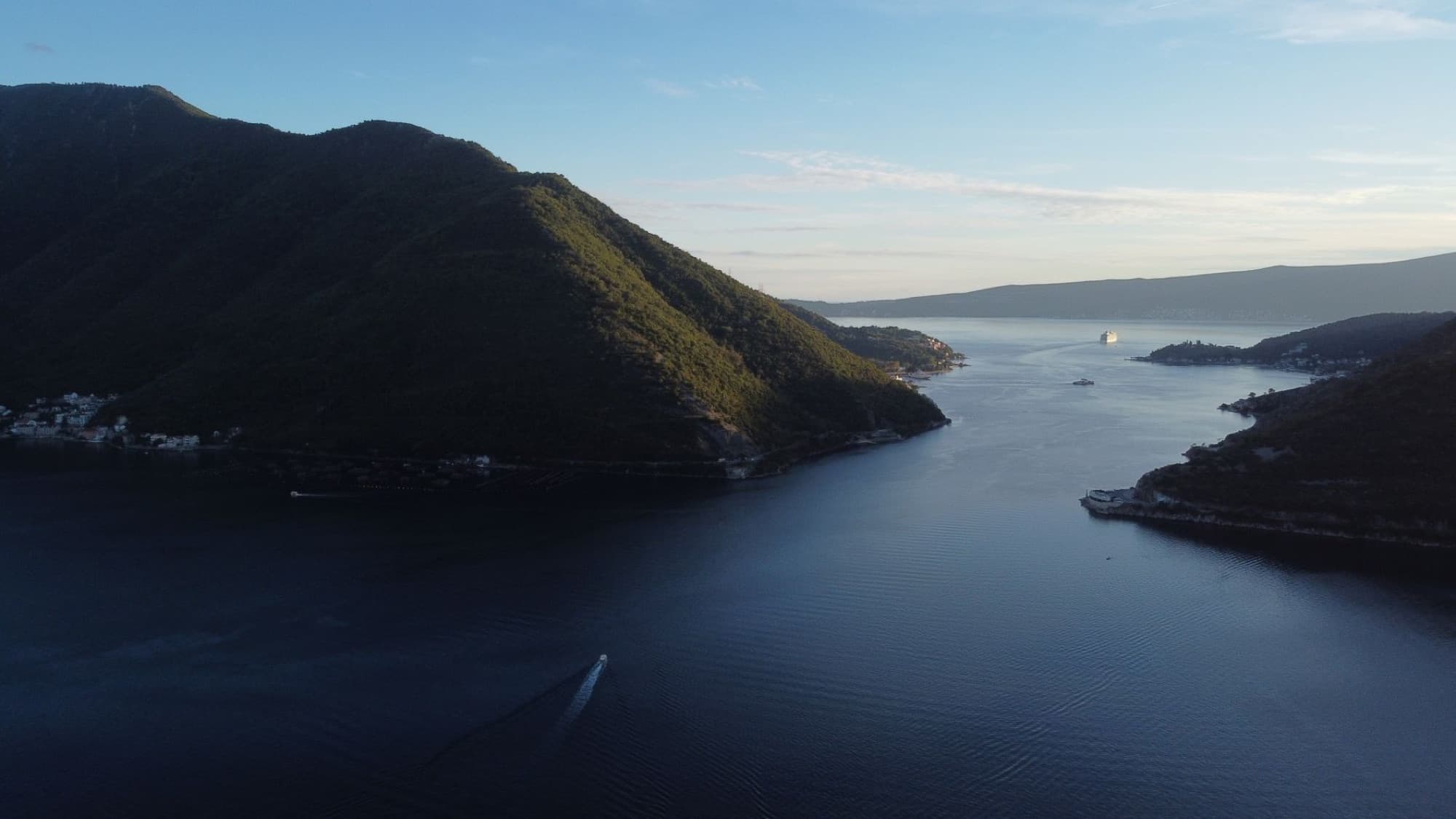 A breathtaking aerial view of Perast Bay, Montenegro with mountains, sea, and a cruise ship at sunset.