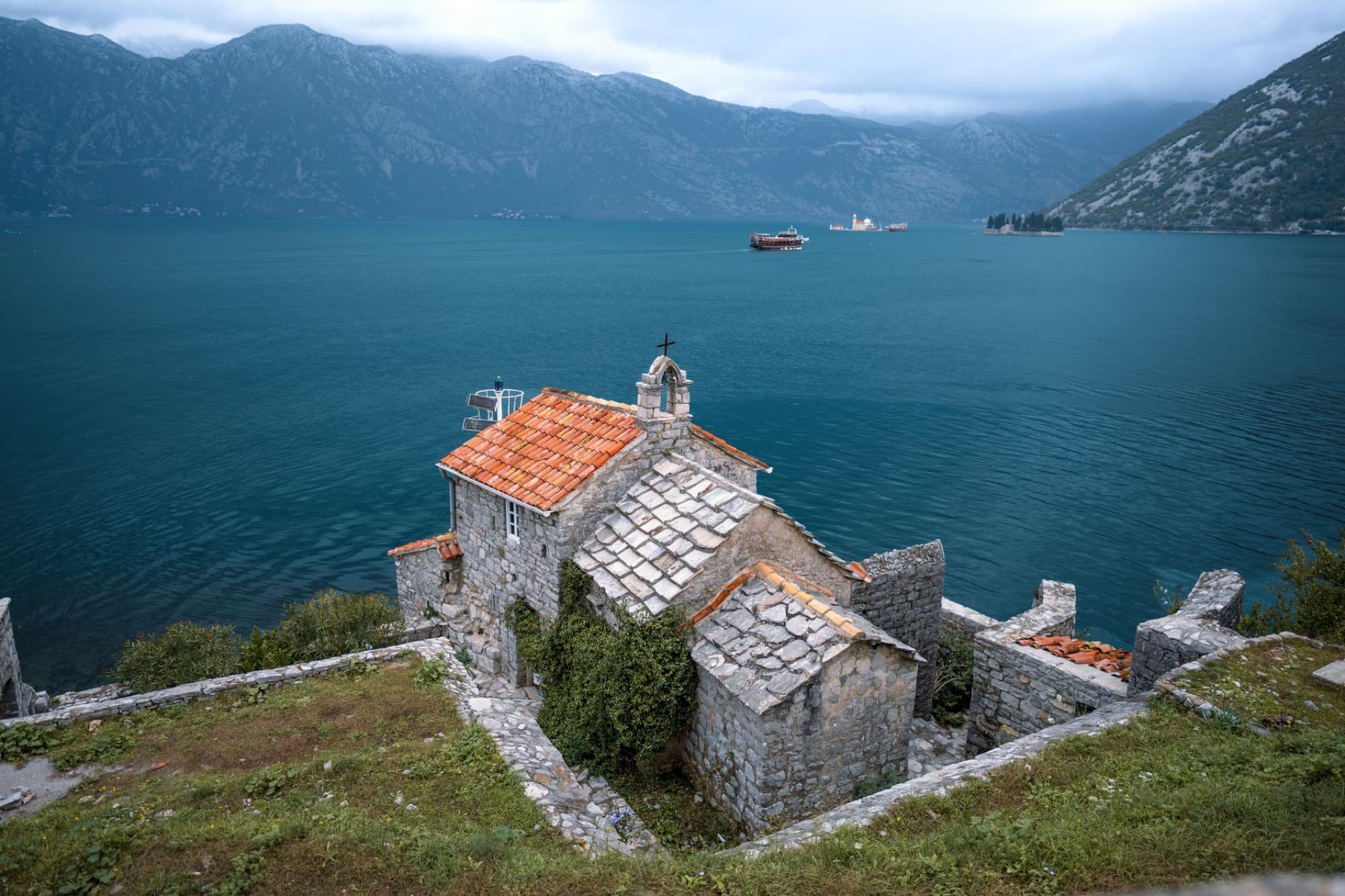 Stone church on Montenegro coast with stunning bay view, ideal for travel and landscape enthusiasts.