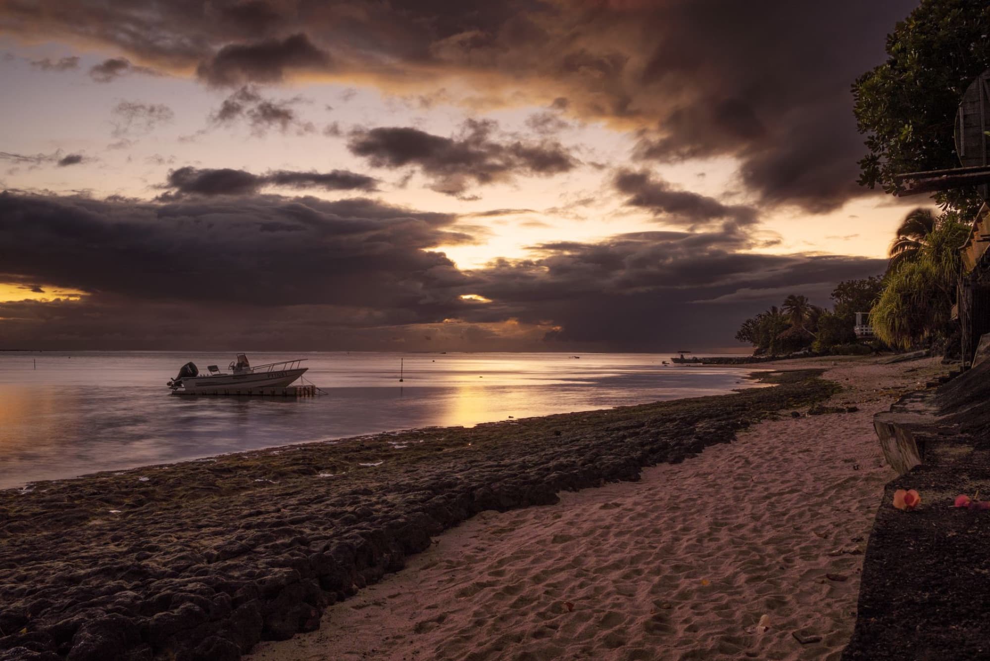 Tranquil sunset over a Moorea beach with a boat and dramatic clouds, capturing a peaceful seascape.