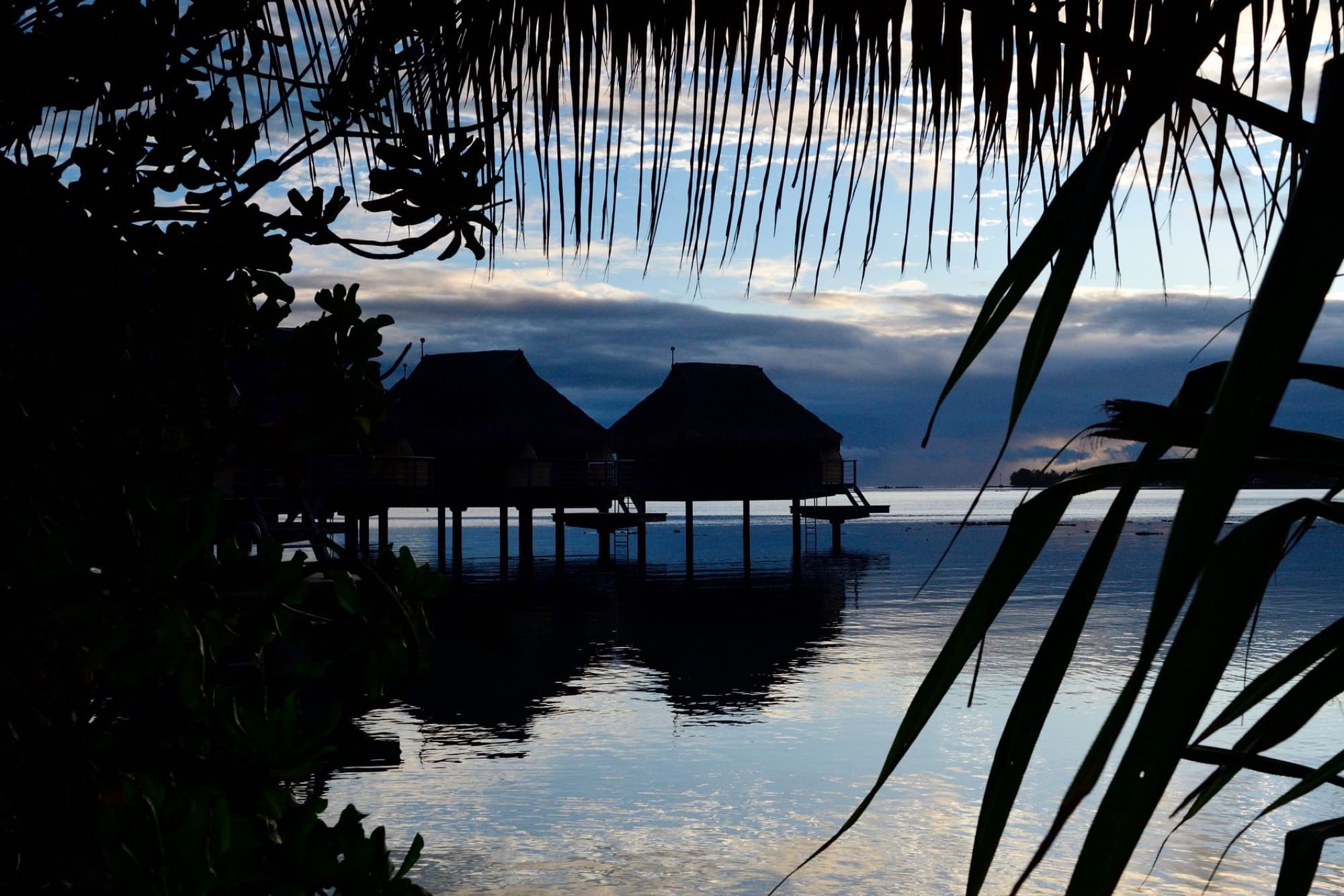 Serene overwater bungalows at sunrise in Moorea, French Polynesia, captured in silhouette against the tranquil lagoon.