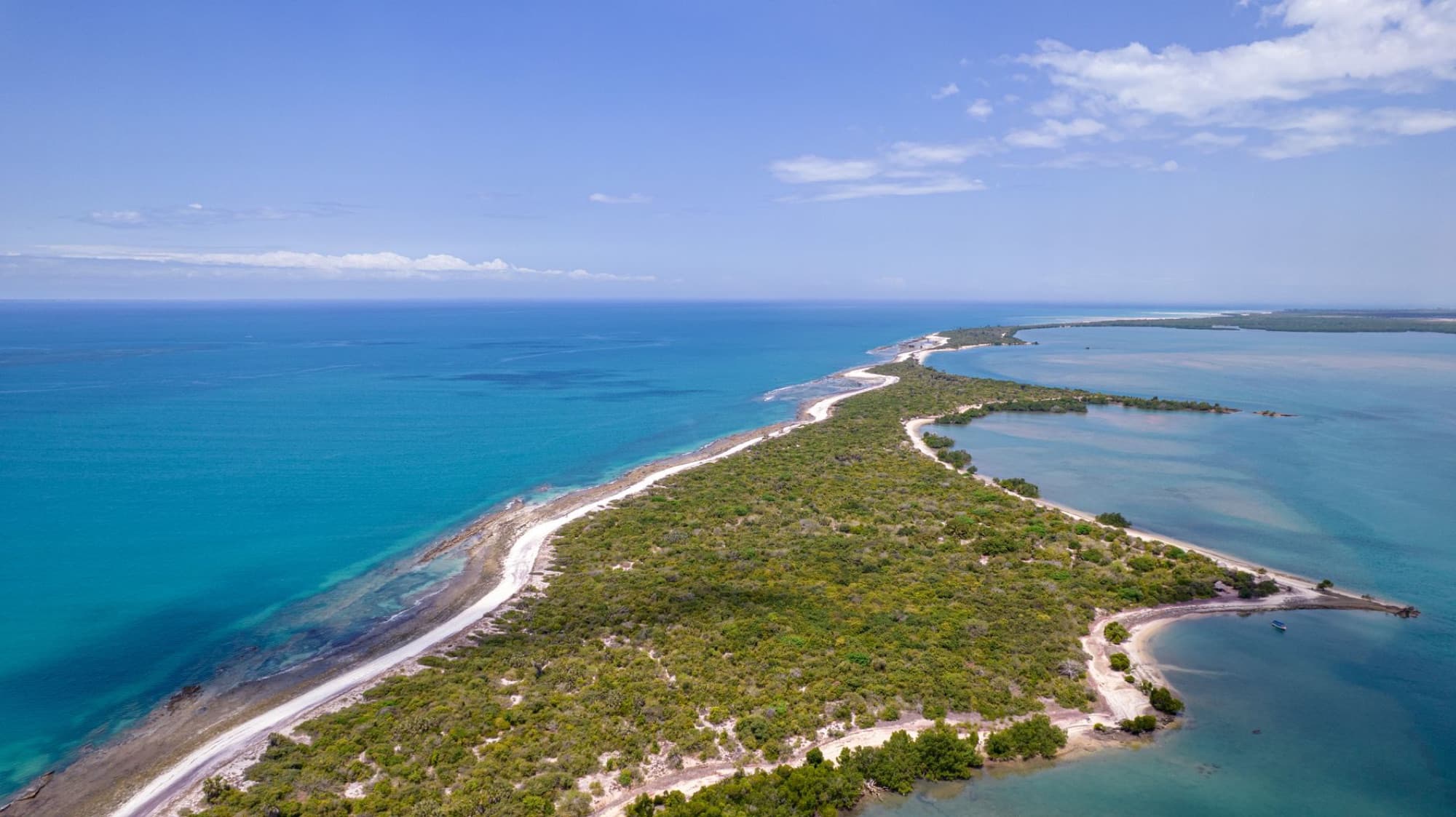 Scenic aerial view of a tropical island with lush greenery and turquoise ocean waters against a clear blue sky.