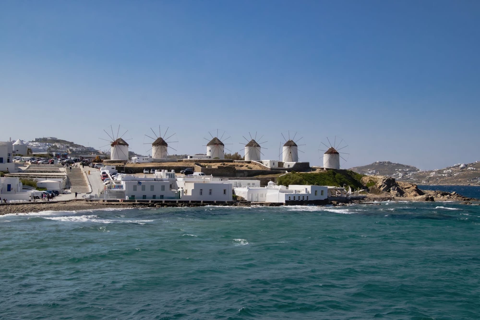 Beautiful view of the famous windmills on Mykonos island's coastline with clear blue skies and sea.