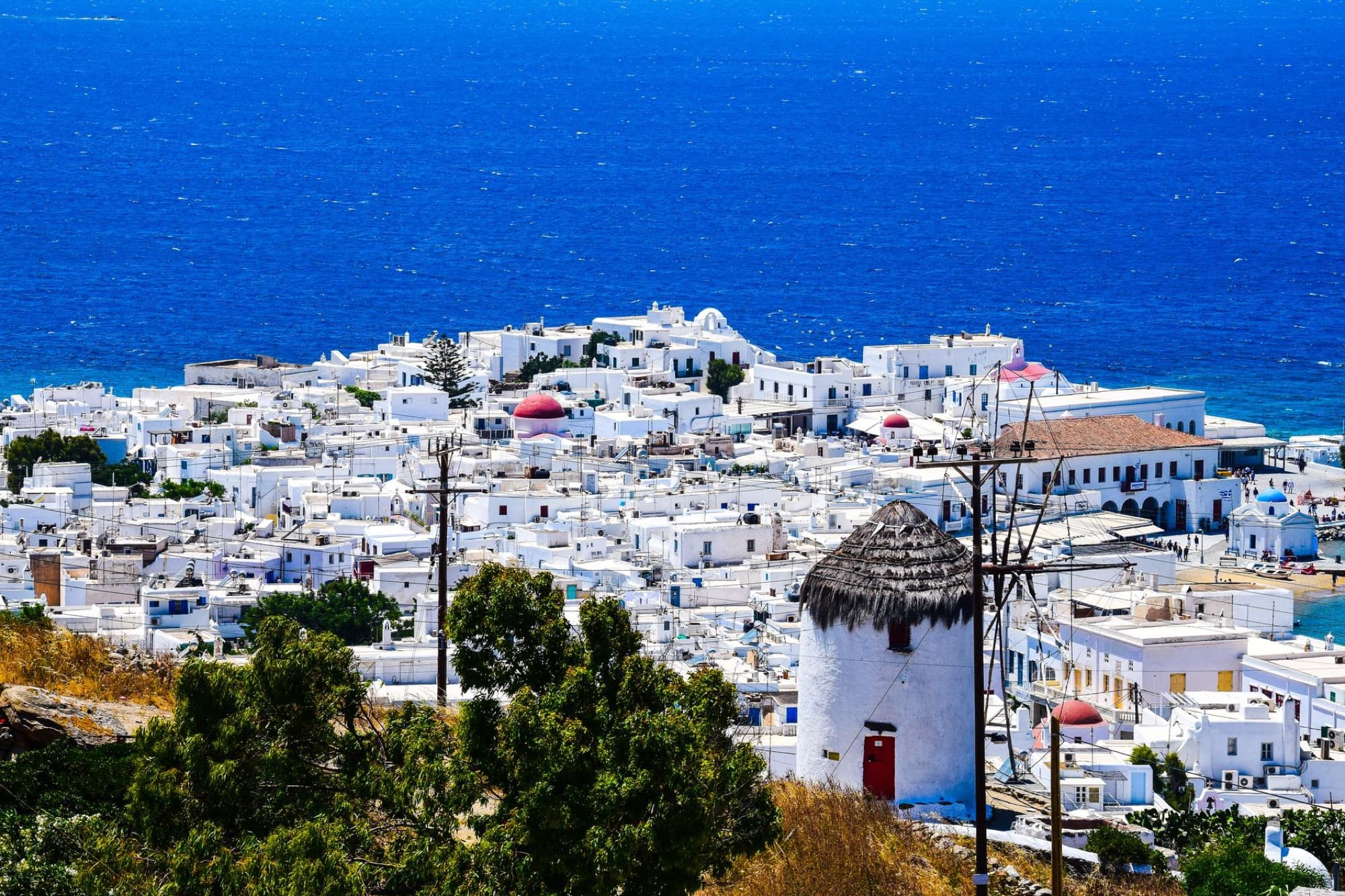 A stunning bird's-eye view of white buildings in Mykonos Town overlooking the blue Aegean Sea.