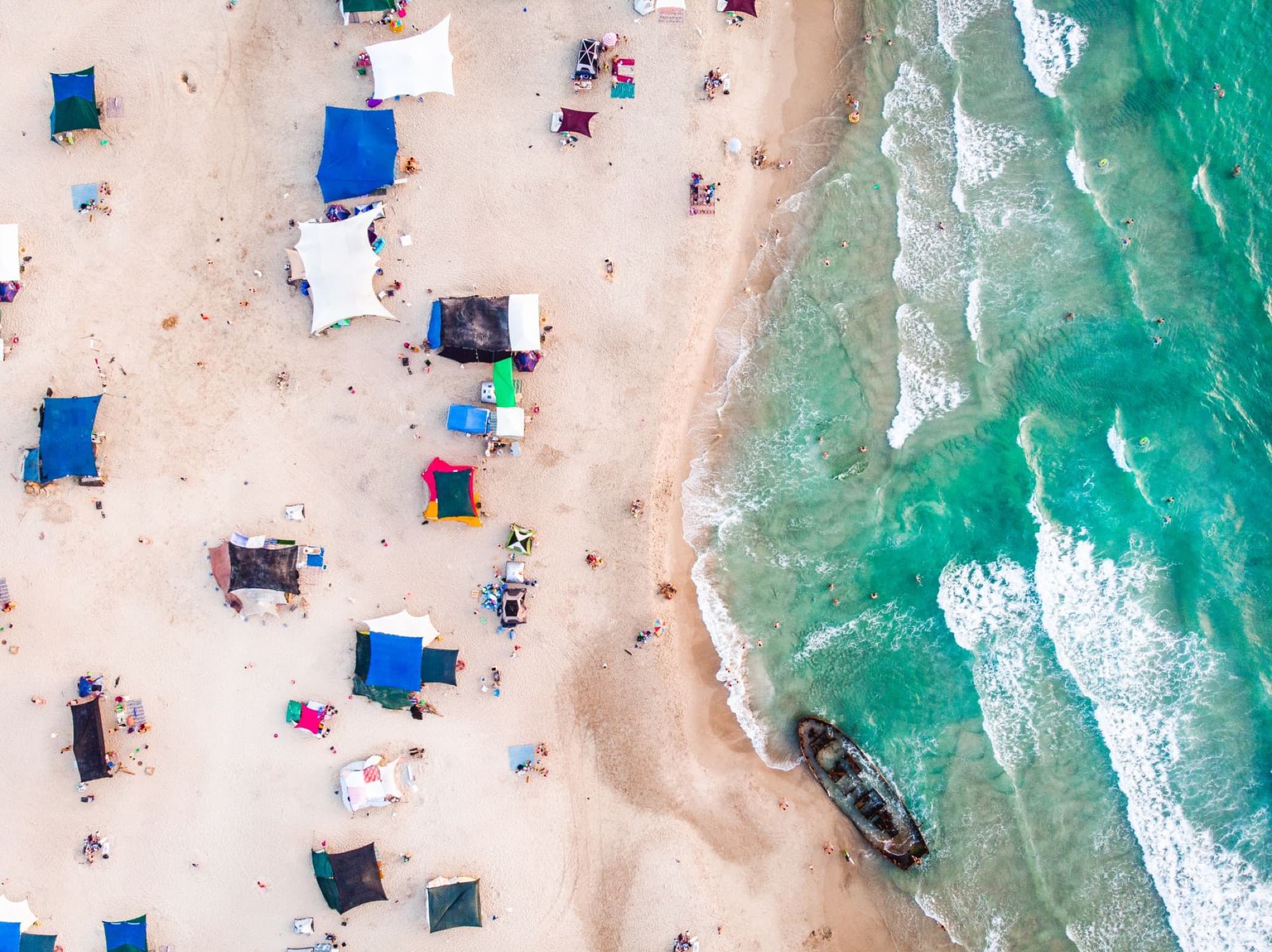 Stunning aerial view of a vibrant and busy beach in Israel, showcasing colorful tents and turquoise waves.