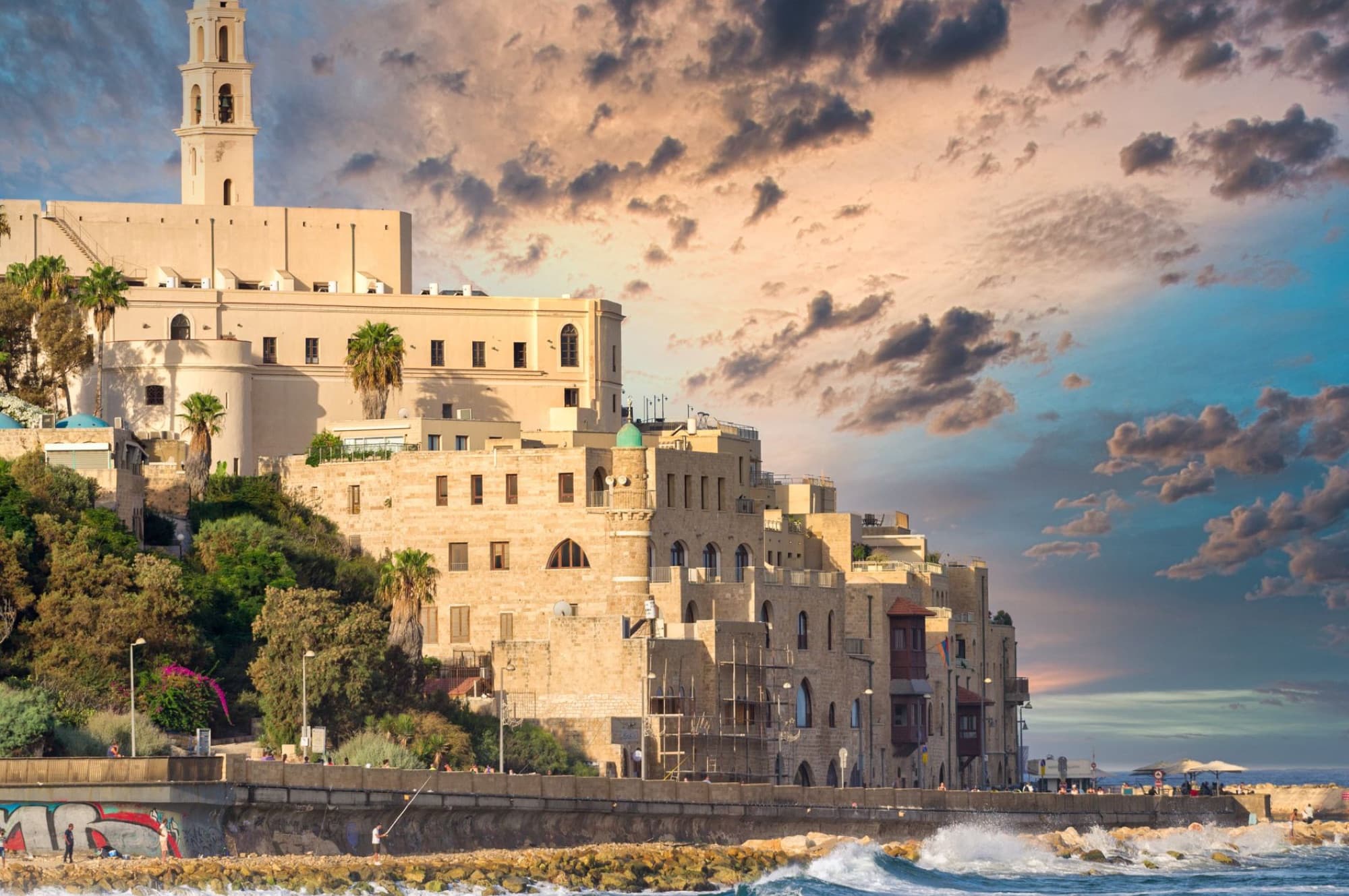 Scenic view of historic city buildings on a Mediterranean waterfront at sunset, showcasing ancient architecture.