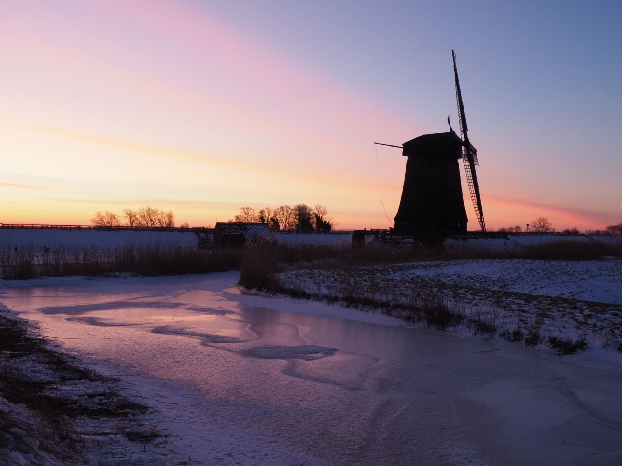 Scenic view of a Dutch windmill during winter sunset with a frozen river in Schermerhorn, Netherlands.
