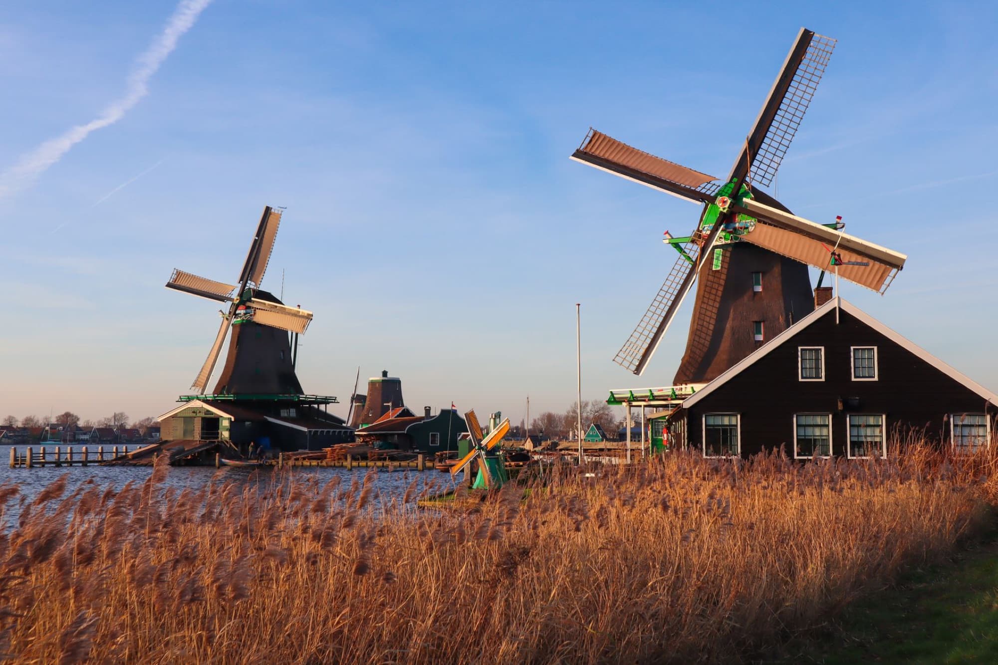 Scenic view of iconic Dutch windmills near water at Zaanse Schans, Netherlands, during sunset.