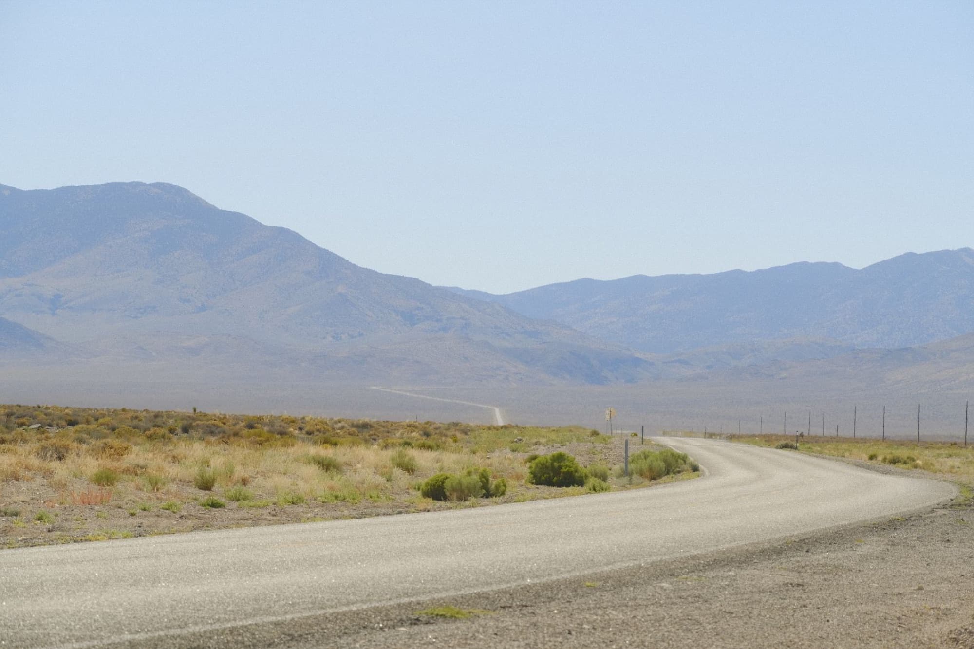 Wide open desert road showcasing the vast Nevada landscape with mountains in the background.