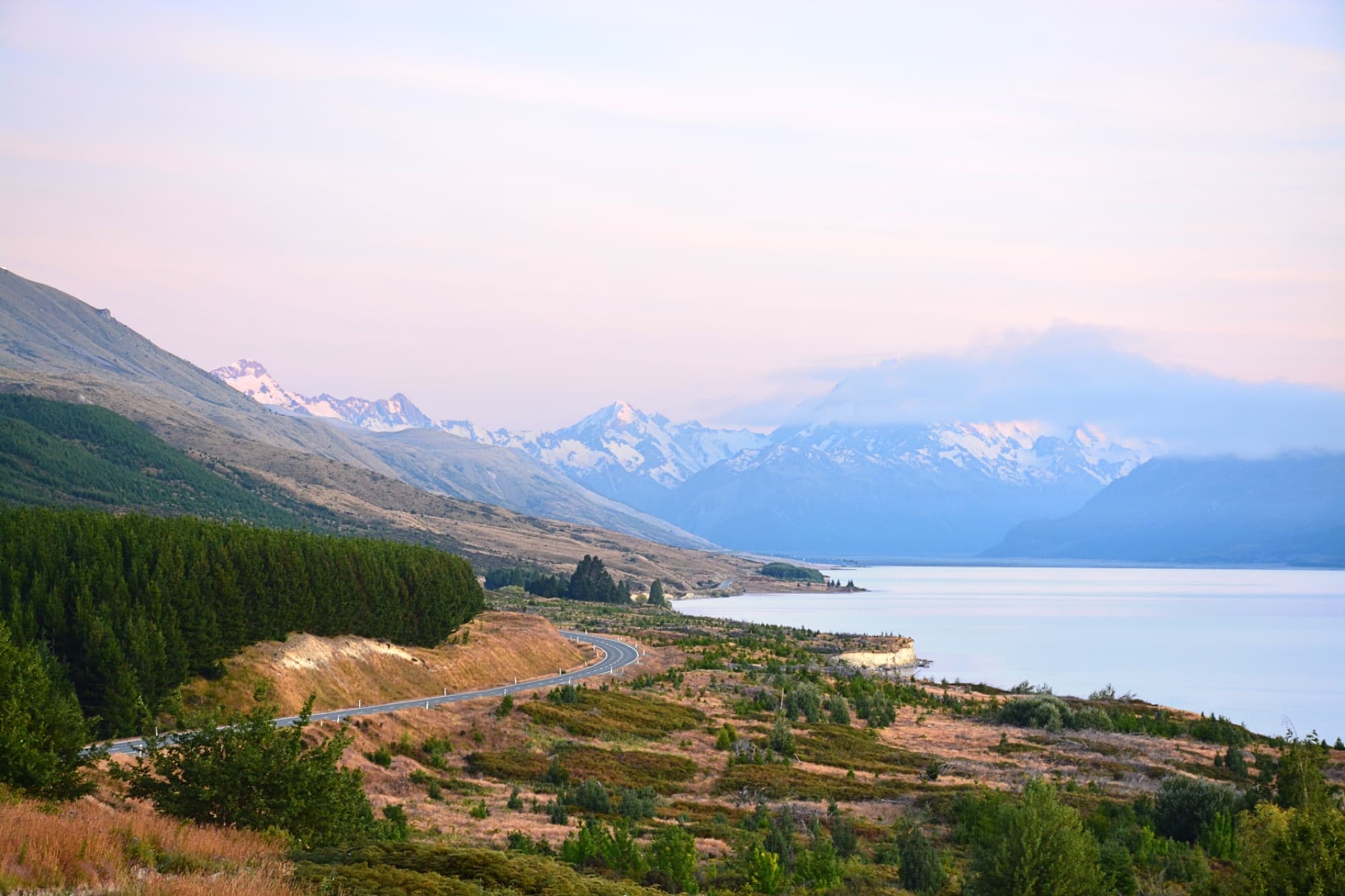 Picturesque landscape of Lake Pukaki with mountains and winding road at sunset in New Zealand.