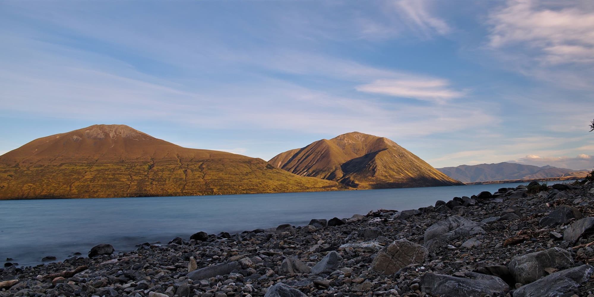 Stunning landscape of Lake Ohau with rocky shoreline and mountains under a clear sky in Canterbury, New Zealand.