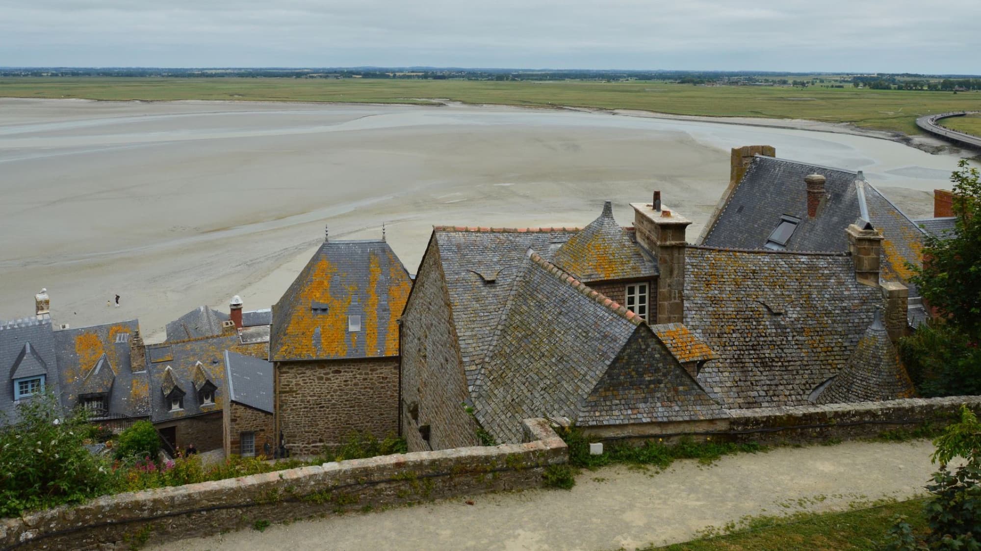 Aerial view of historic rooftops at Le Mont-Saint-Michel with scenic tidal flats in Normandy, France.
