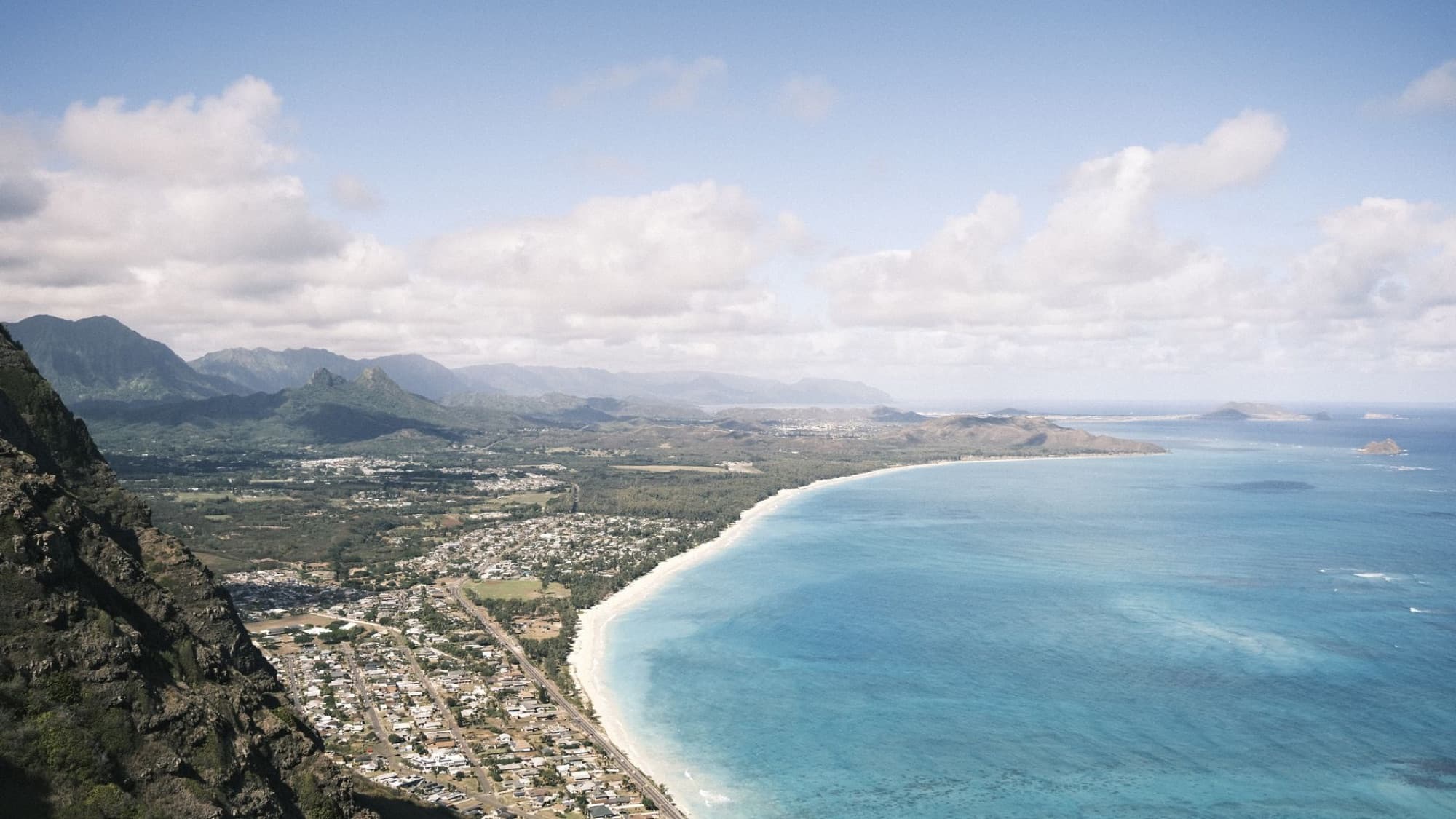 Sweeping aerial view of Oahu coastline with vibrant ocean, lush mountains, and coastal towns.