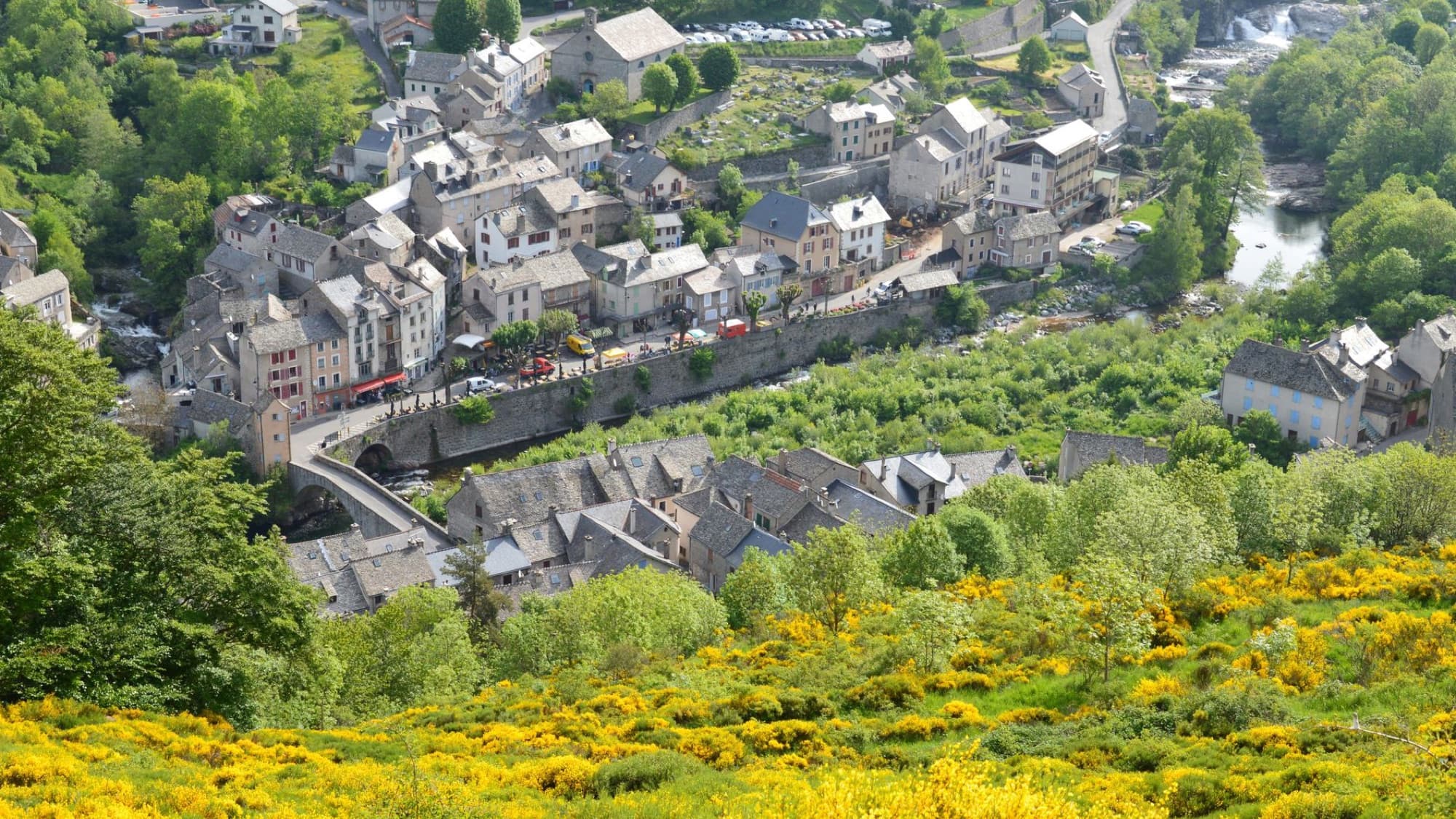 Charming aerial view of Pont de Montvert village in Occitanie, France, amidst lush greenery.