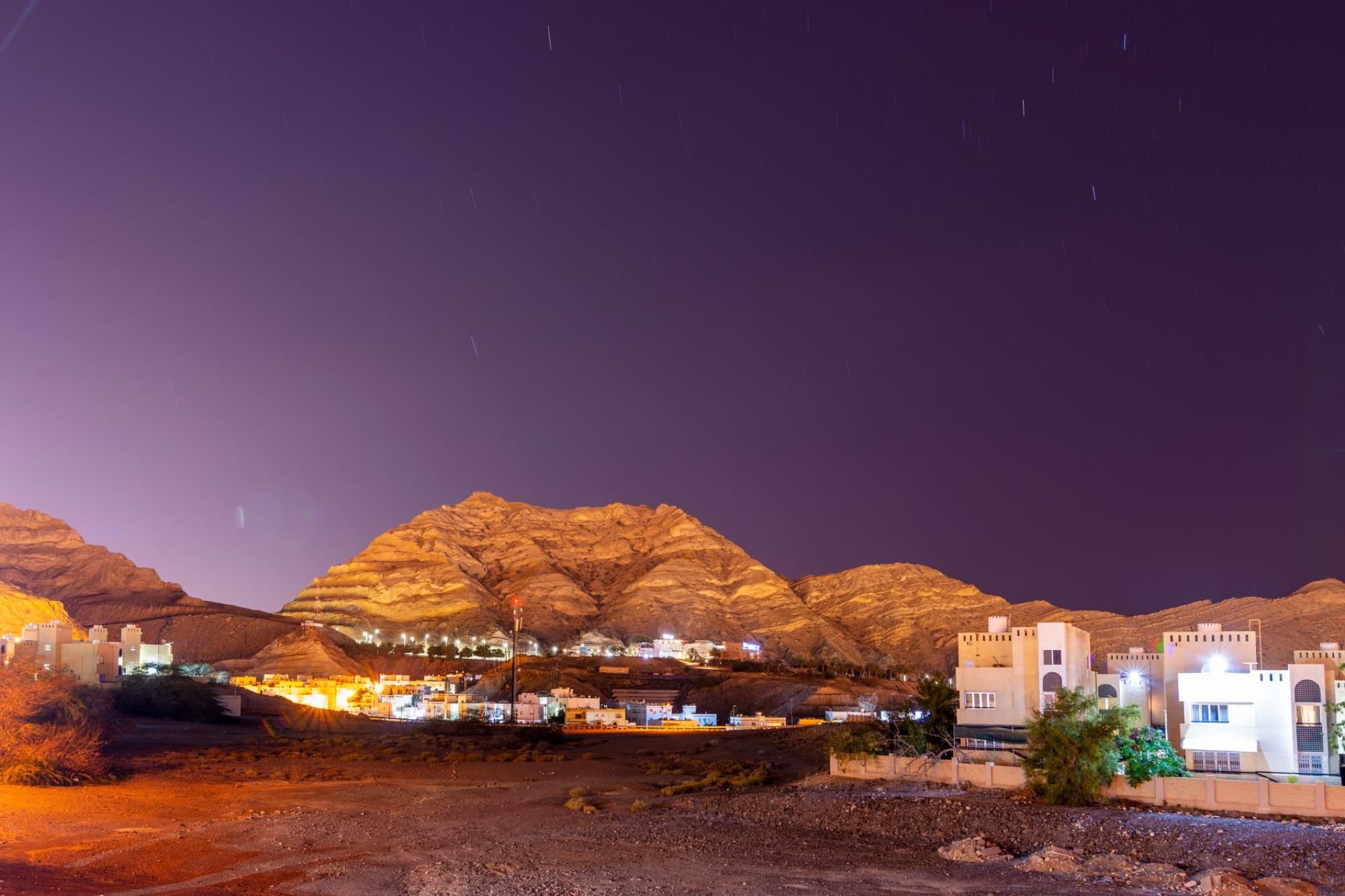 Scenic night landscape of a town in Oman with illuminated buildings against mountains.
