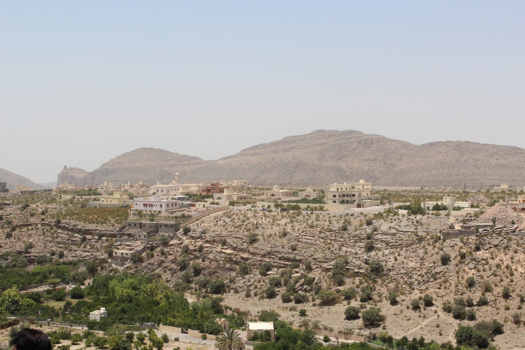 Panoramic view of a village in Ad Dakhiliyah, Oman, surrounded by arid mountains and desert terrain.