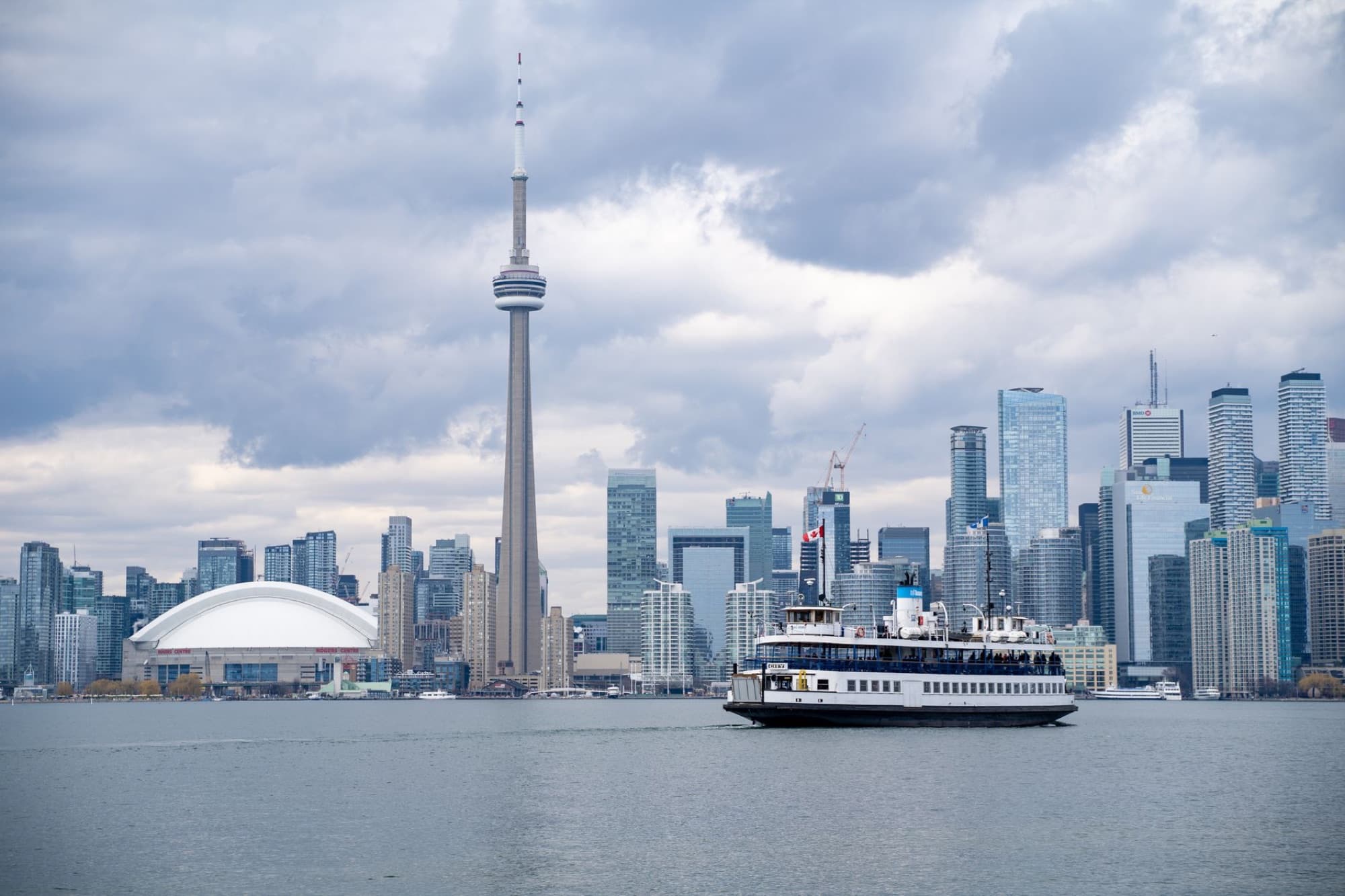 Iconic view of Toronto skyline featuring the CN Tower and a ferry on Lake Ontario.