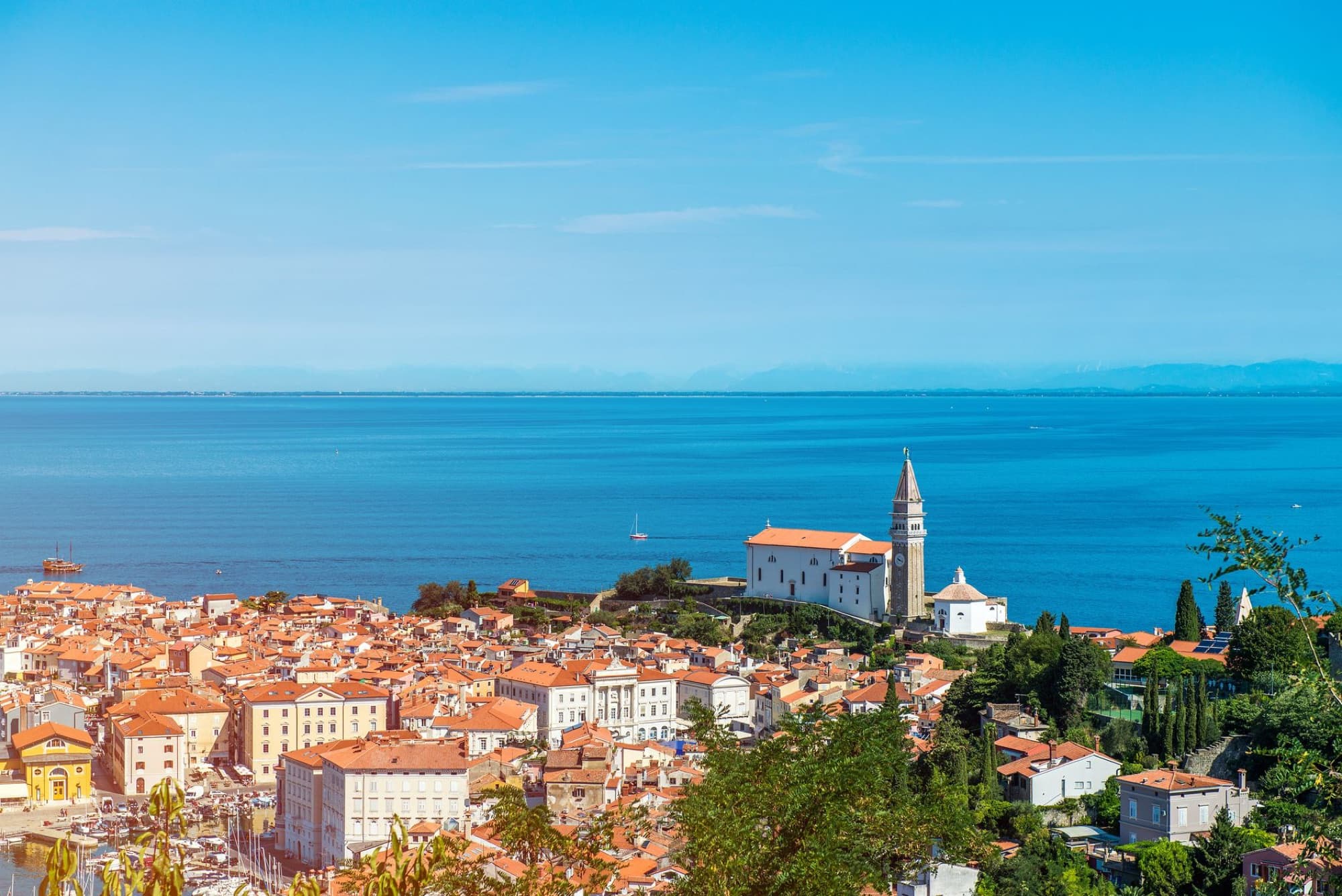 Scenic aerial view of a Mediterranean coastal town with a prominent church by the blue sea, under a clear sky.