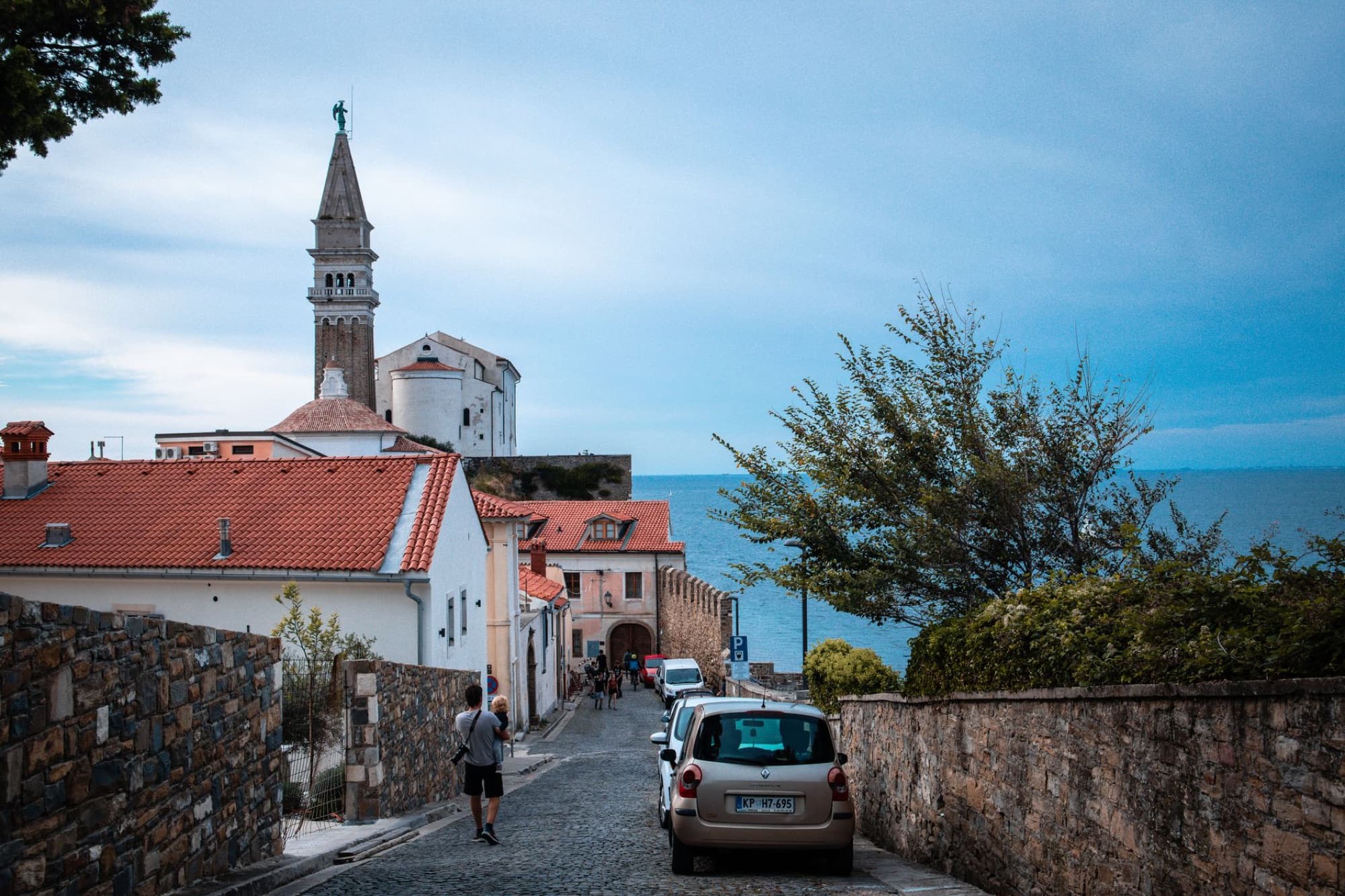 Explore the scenic street of a coastal town with a historic church tower in the background, ideal for tourism and architecture lovers.