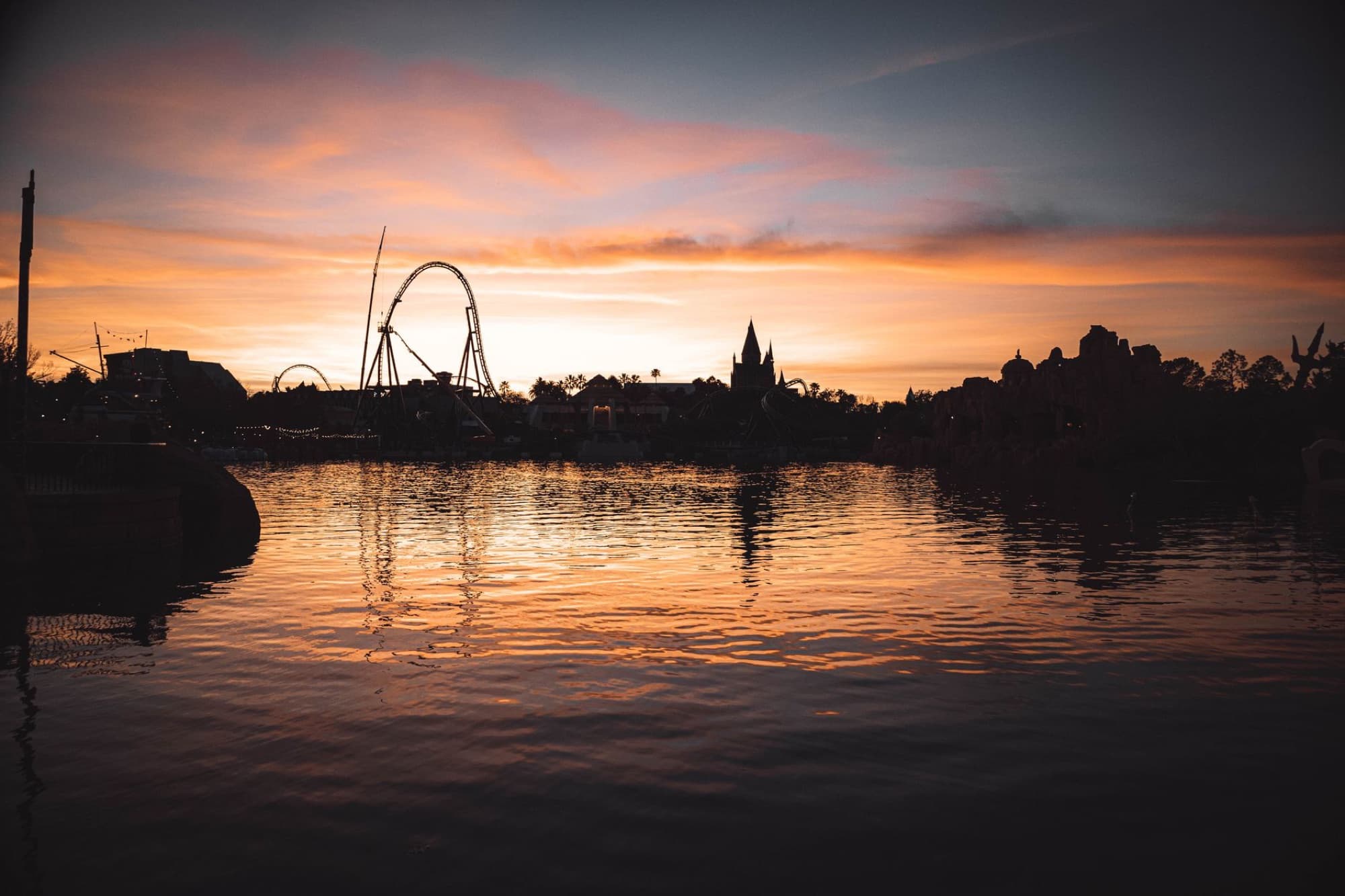 Dramatic sunset reflection on a lake with silhouetted roller coaster and skyline in Orlando.